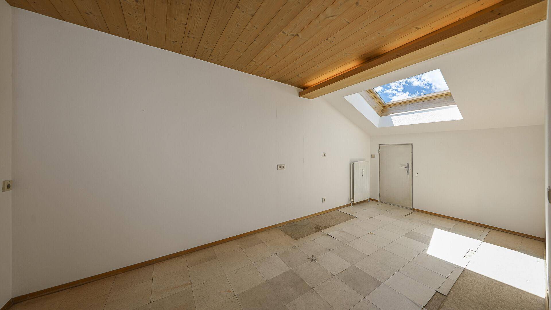 Leerer Dachraum mit Holzdecke, Dachfenster und unfertigem Bodenbelag.