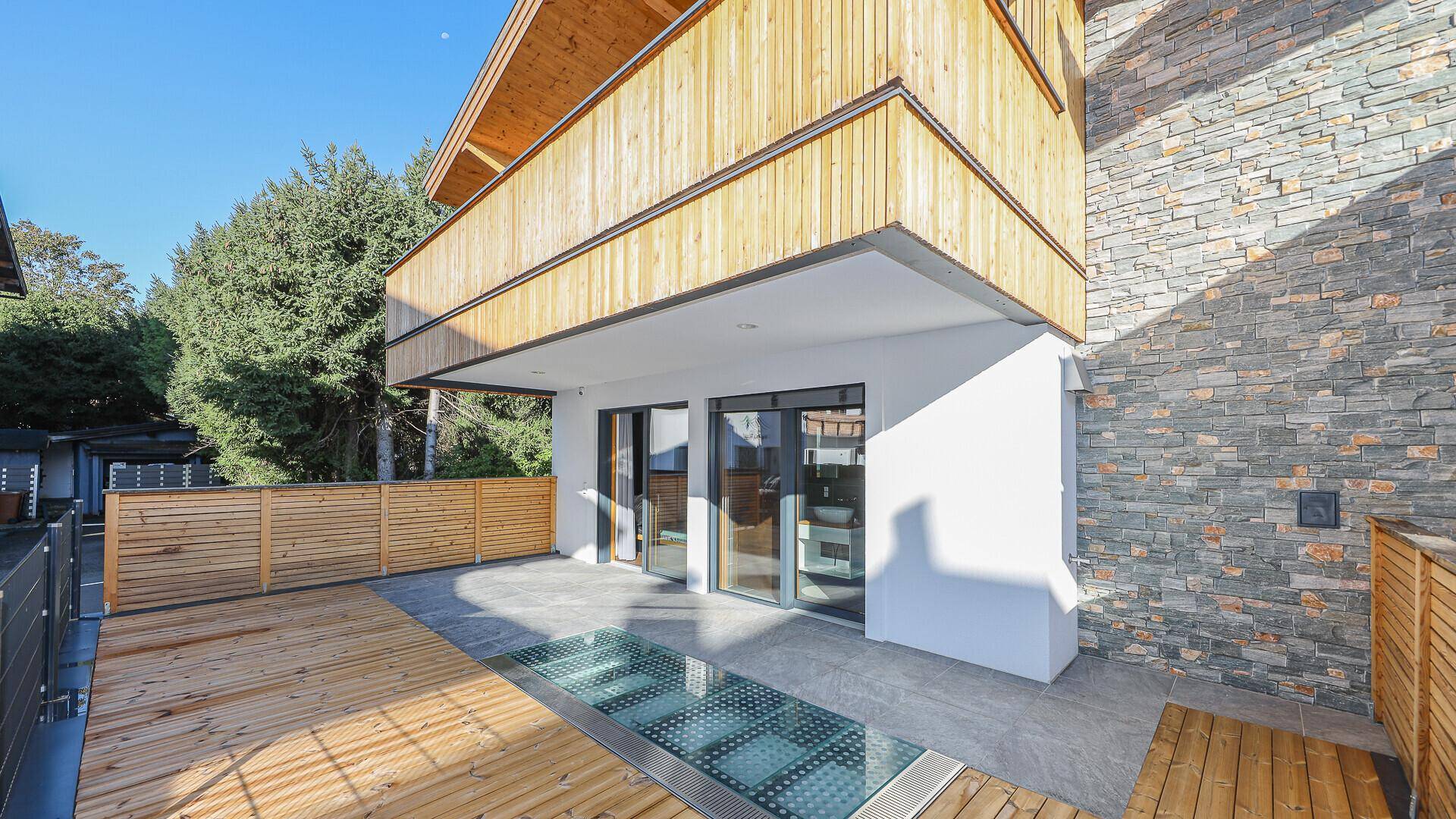 Geräumige Terrasse mit Holzboden und Glasboden-Element, umgeben von Natursteinwand.