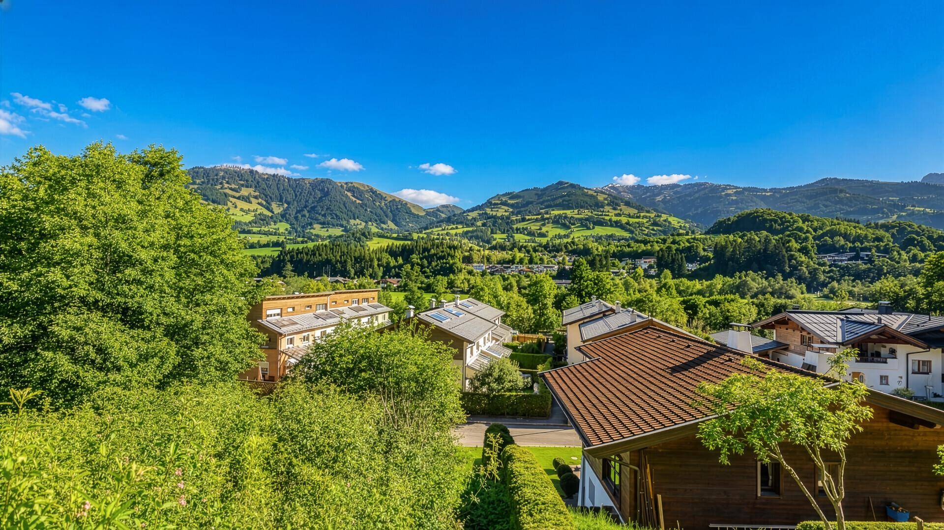 Weitblick über eine Siedlung in einem grünen Tal mit sanften Hügeln und Bergen.