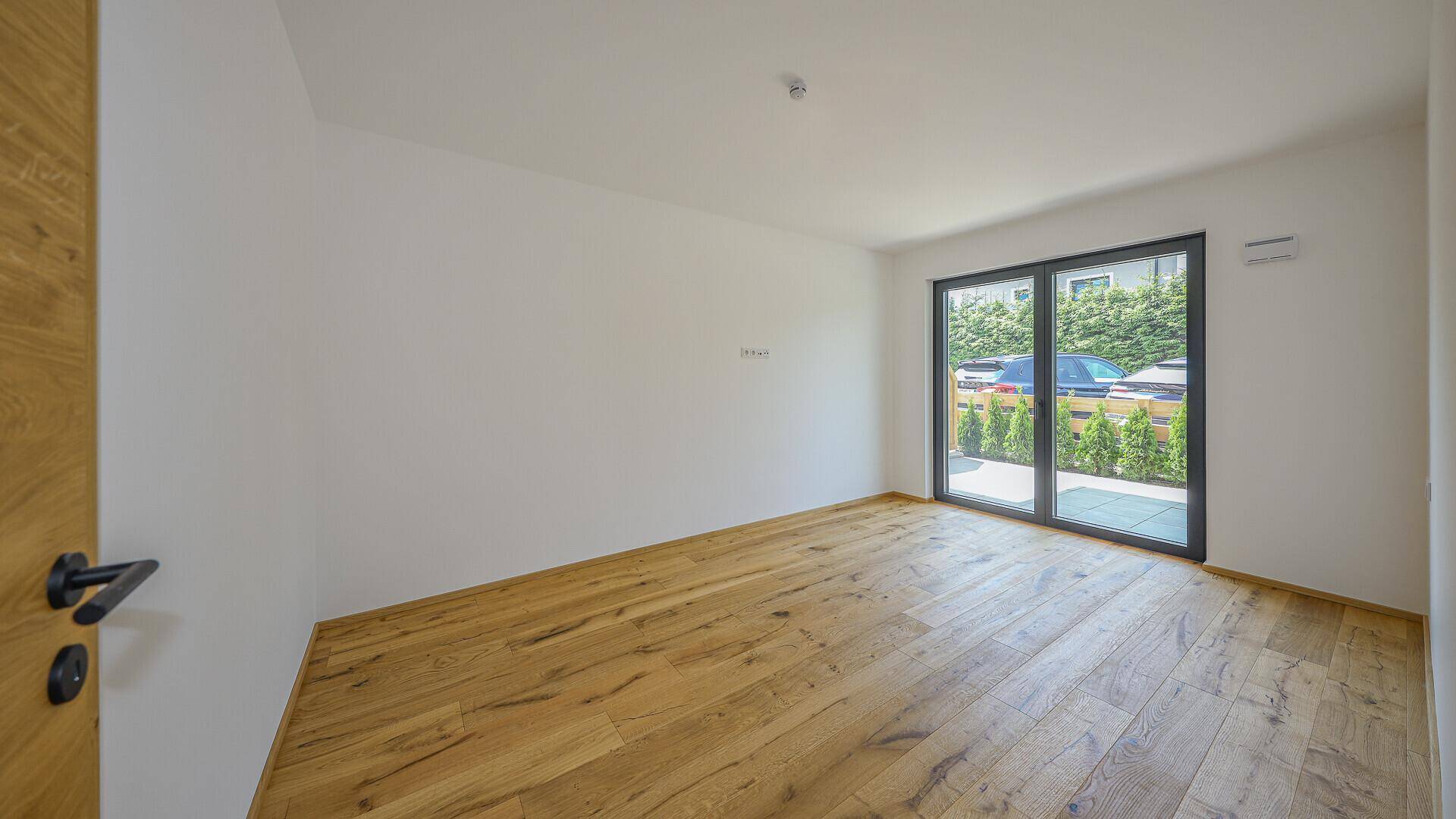 Heller, unmöblierter Raum mit Holzboden und Zugang zu einem privaten Außenbereich.
