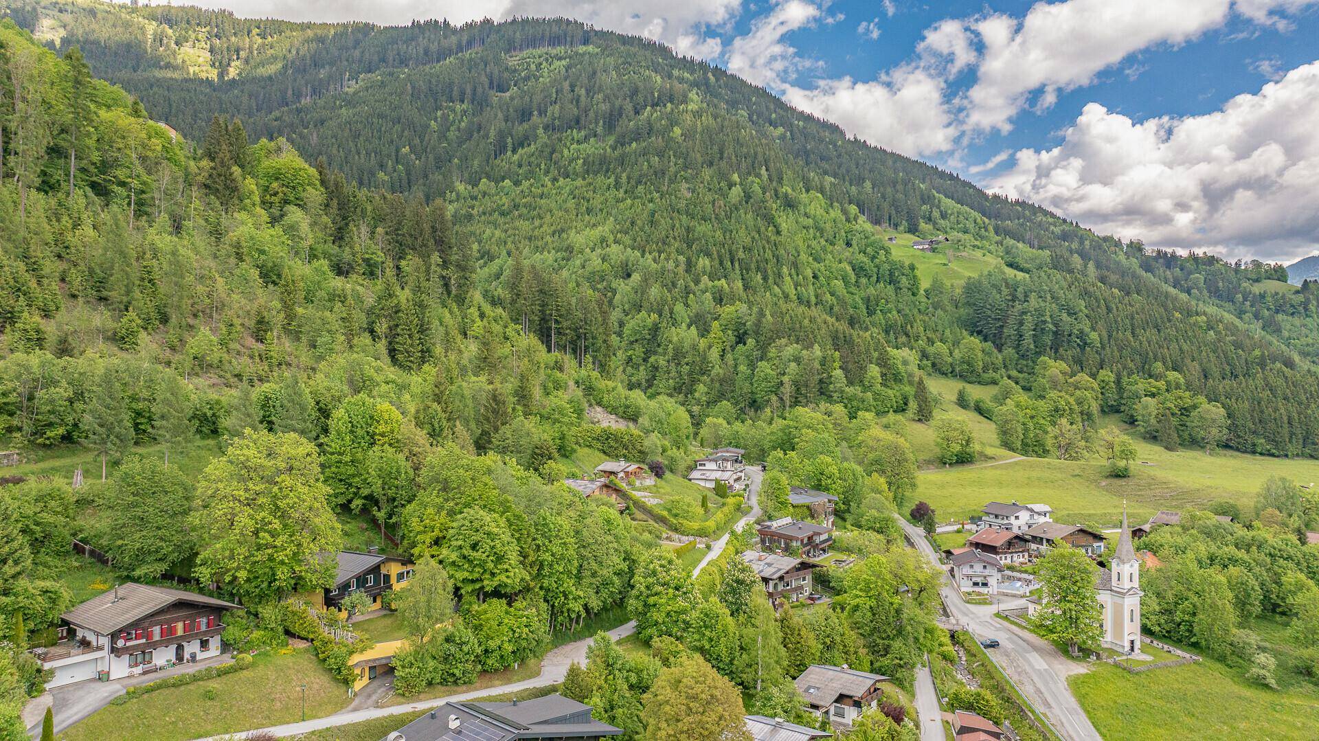 Luftaufnahme einer malerischen Siedlung in einer grünen Berglandschaft mit Häusern und Kirche.