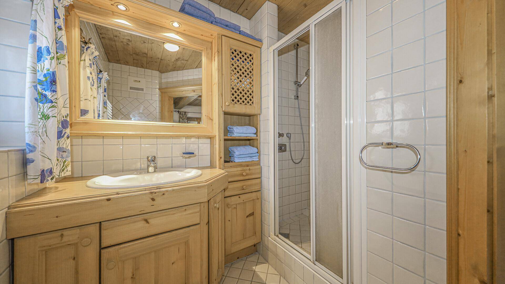 Traditionelles Badezimmer mit Dusche, Holzwaschtisch und hellen Fliesen.