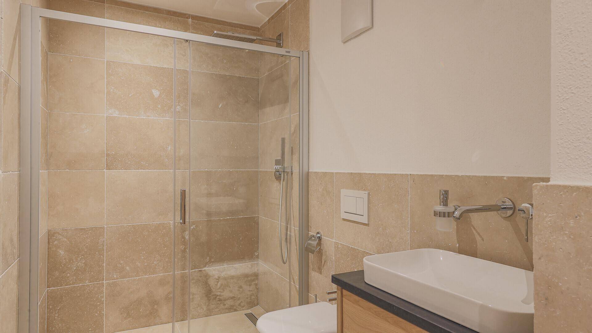 Modernes Badezimmer mit begehbarer Dusche, Waschbecken und beigefarbenen Fliesen.
