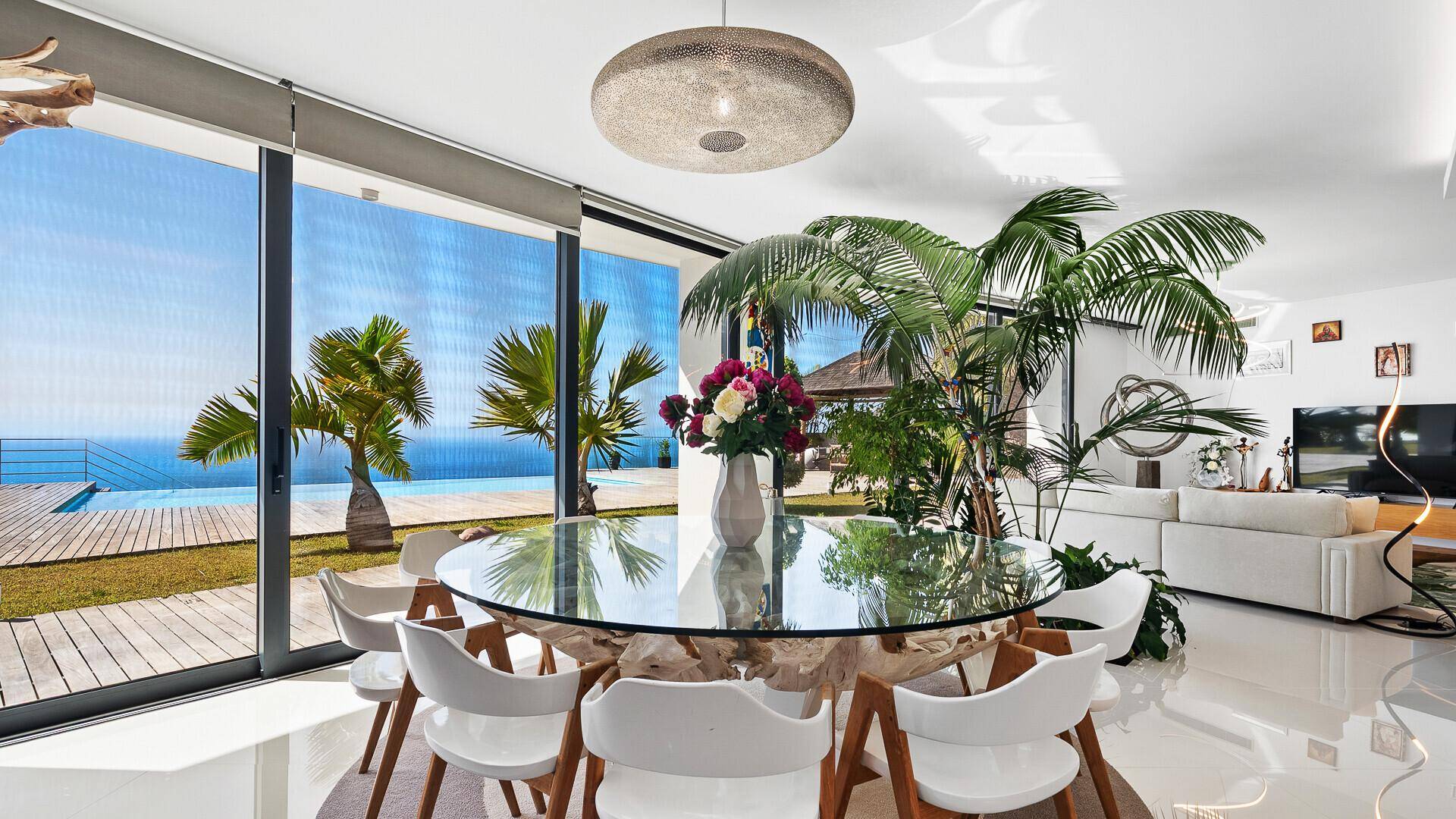 Eleganter Essbereich mit Glastisch und modernen Stühlen, bietet einen atemberaubenden Blick auf den Pool und das Meer.
