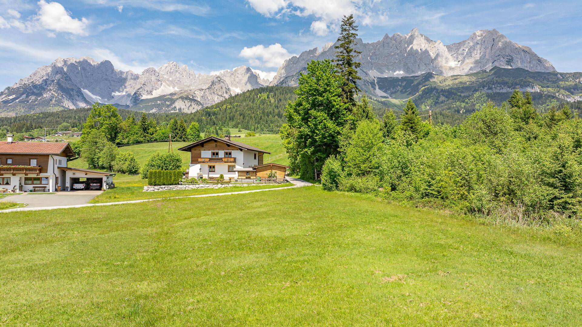 Idyllische Alpenlandschaft mit traditionellen Häusern, umgeben von grünen Wiesen und bewaldeten Hügeln.