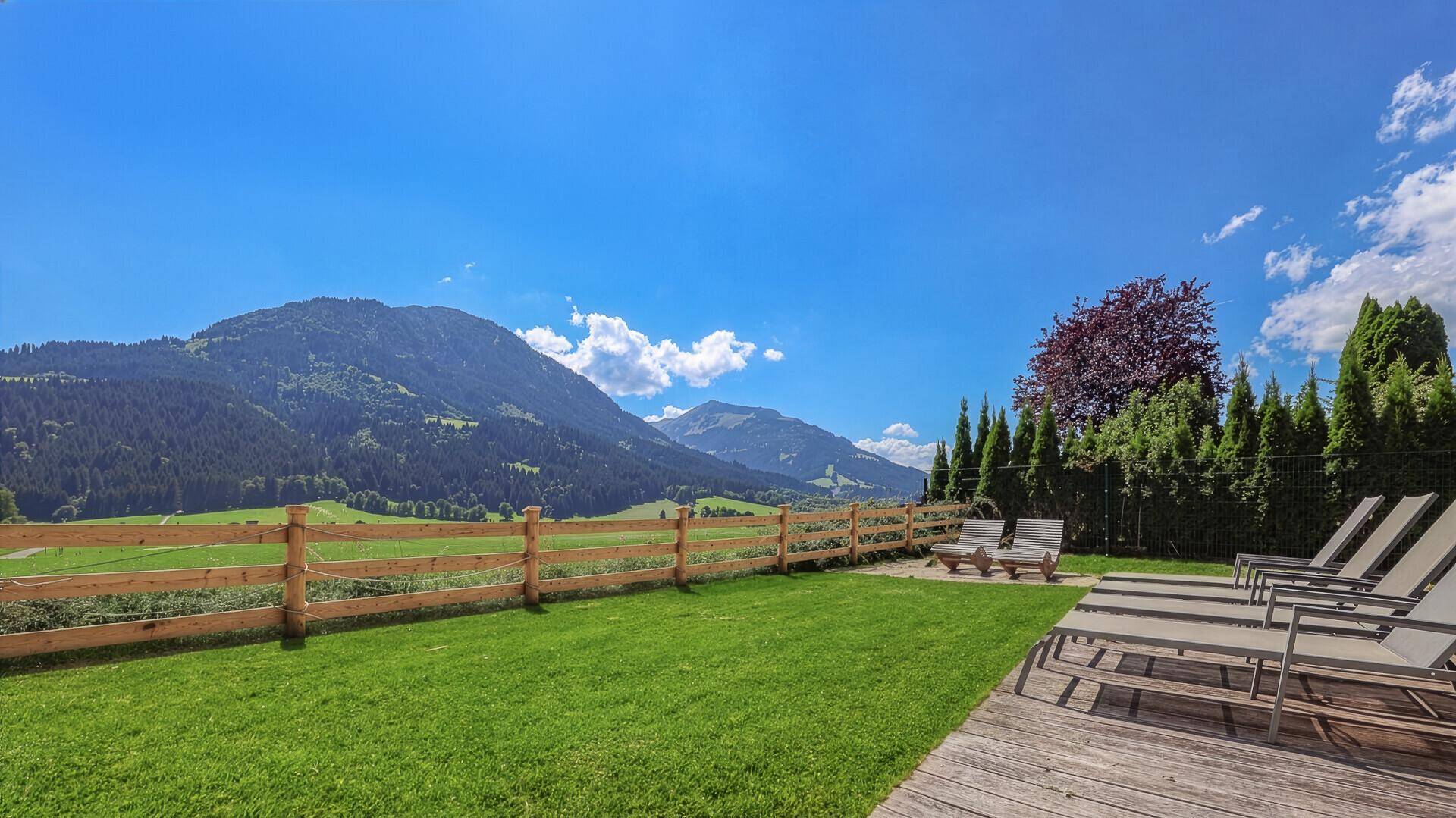 Gepflegter Garten mit Rasenfläche, Liegestühlen und weitem Blick auf die umliegende Berglandschaft.