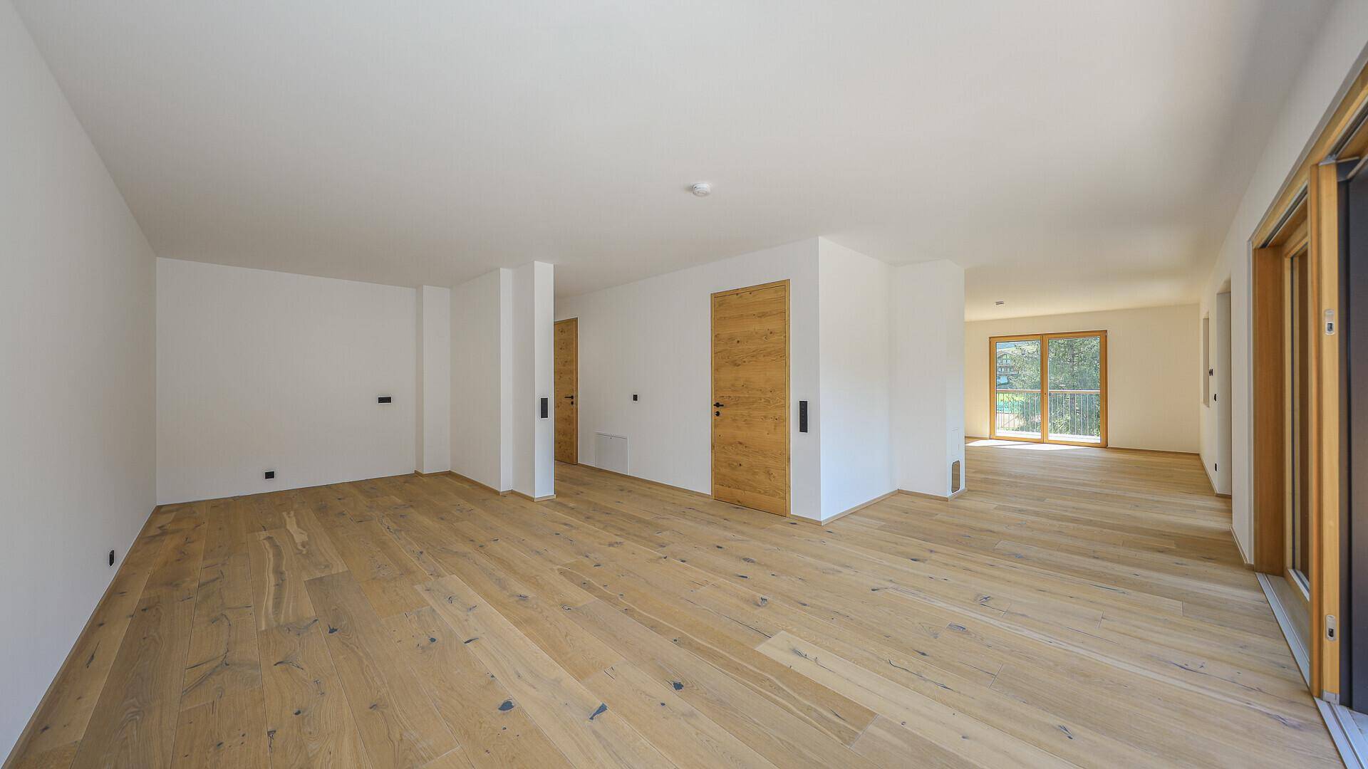 Heller, leerer Wohnbereich mit Holzboden und Zugang zu einem Balkon.