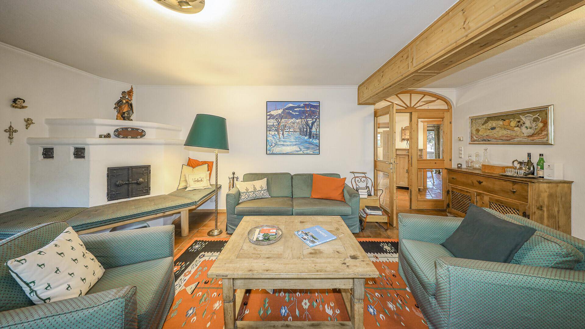 Gemütliches Wohnzimmer mit Kachelofen, Holztisch und Blick auf den Essbereich.