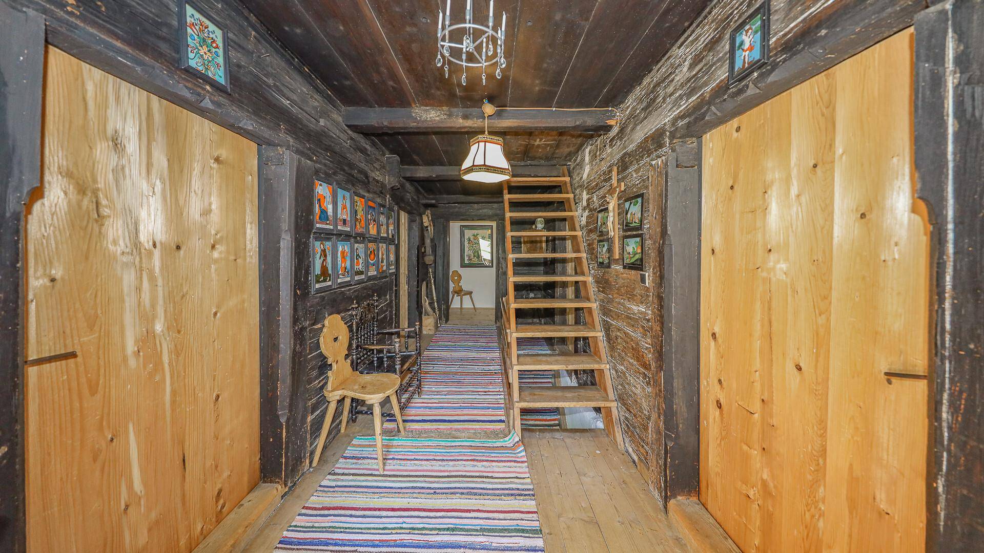 Langer Flur mit Holztreppe, dunklen Holzwänden und traditionellen Dekorationen.