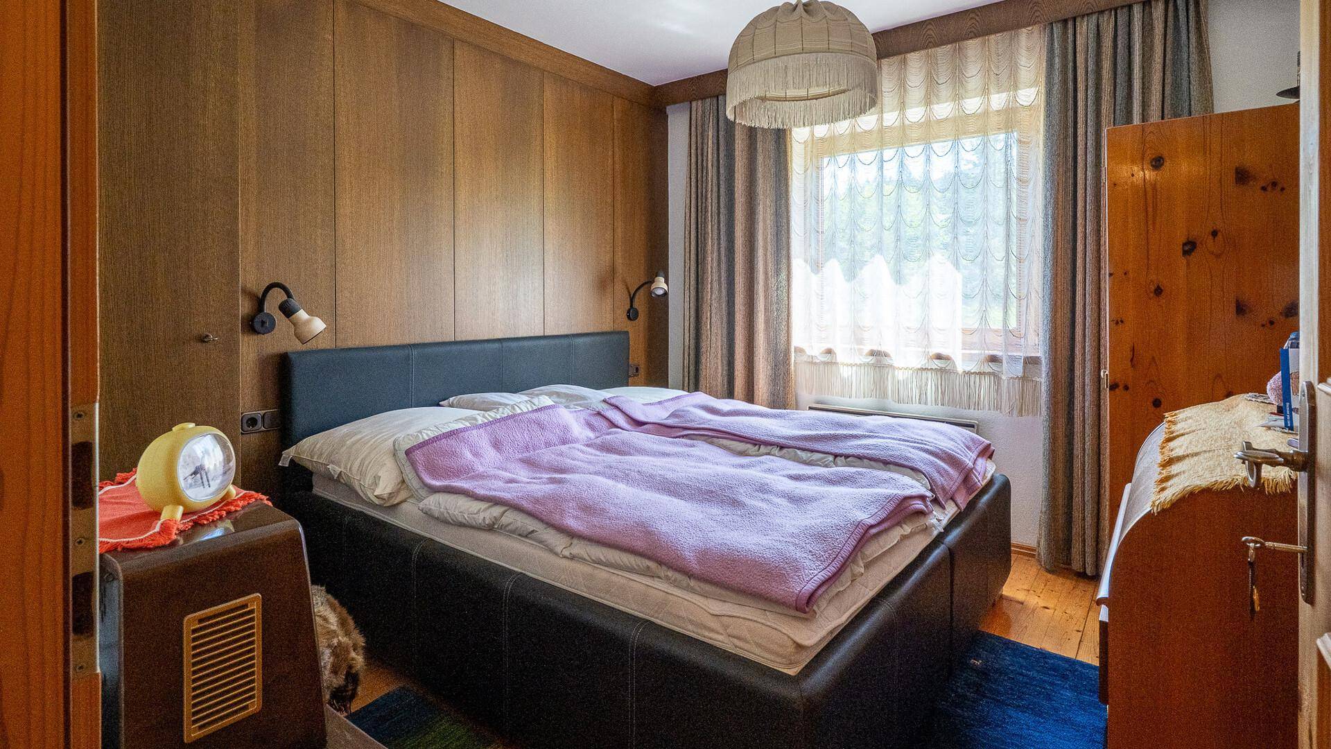 Schlafzimmer mit Holzvertäfelung, Doppelbett und Fenster mit Vorhängen, im traditionellen Stil.