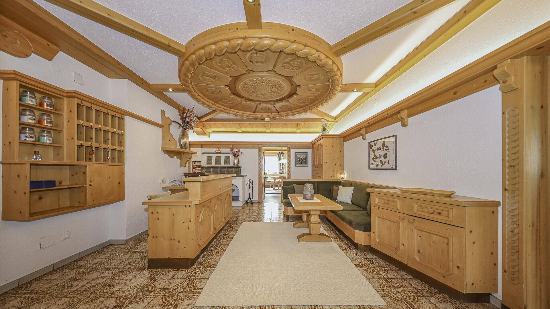 Traditioneller Empfangsbereich im alpinen Stil mit Holzeinbauten, geschnitzter Decke und gemustertem Fliesenboden.