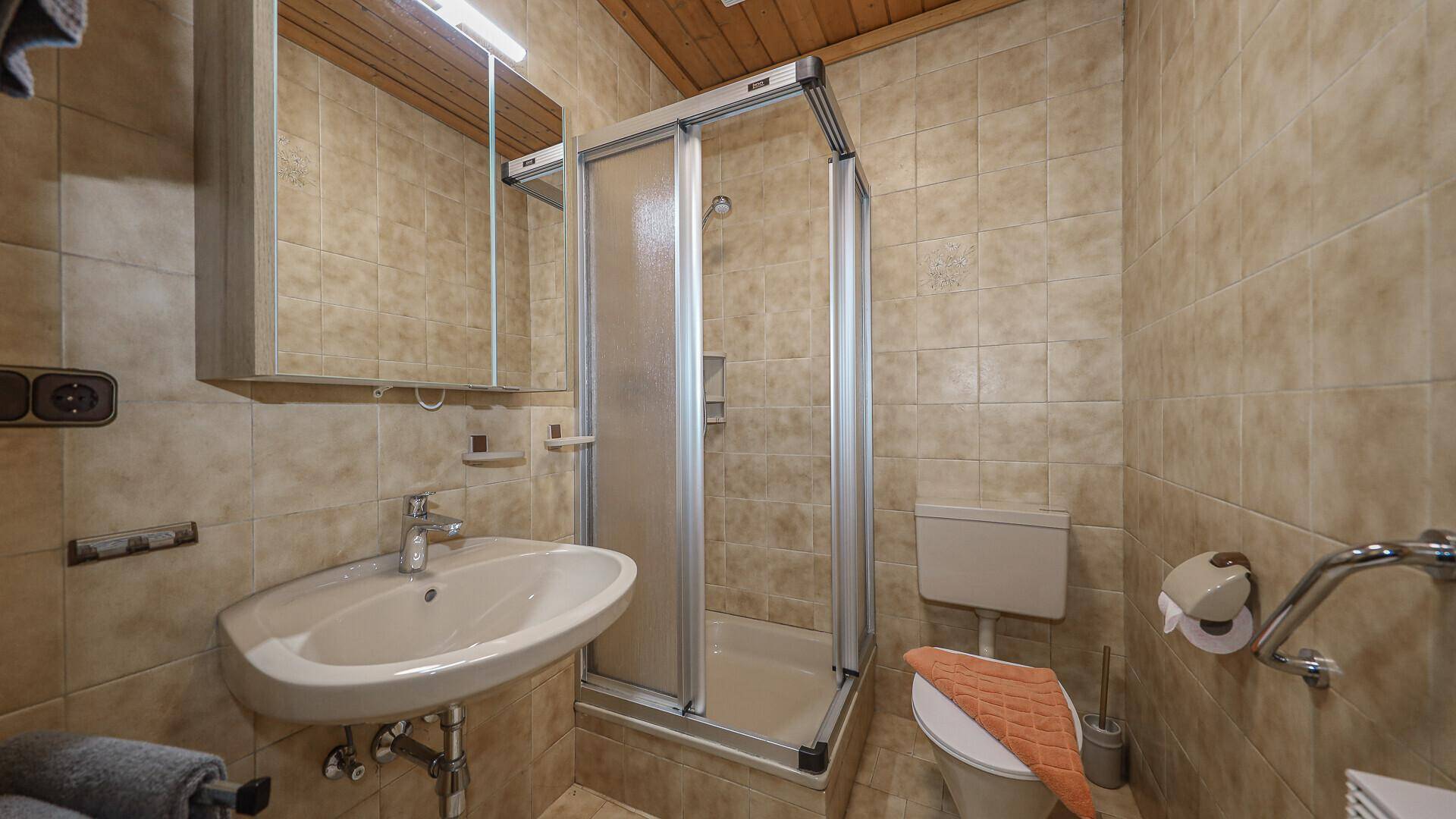 Funktionales Badezimmer mit Duschkabine, Einzelwaschbecken und beigefarbenen Fliesen.