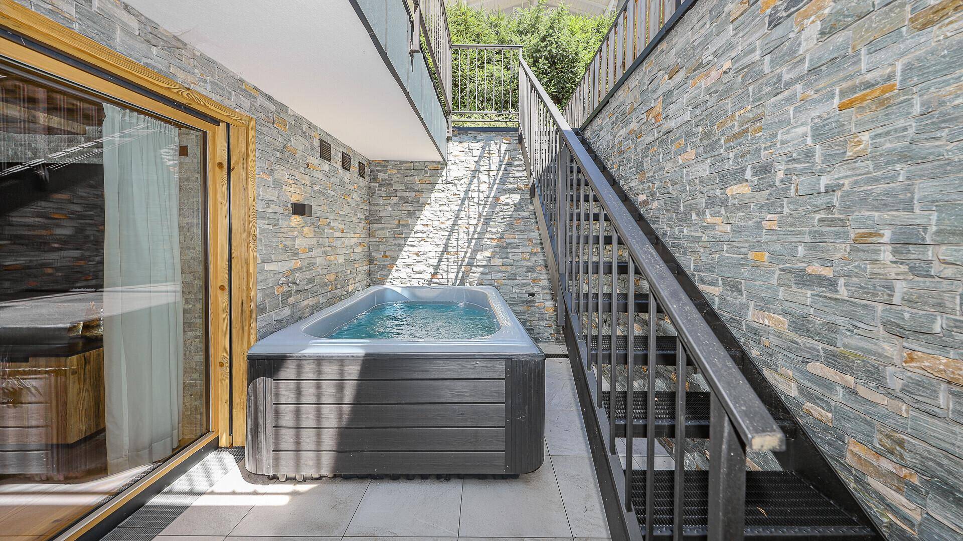 Außenbereich mit Whirlpool und Steintreppe, umgeben von Steinmauern.