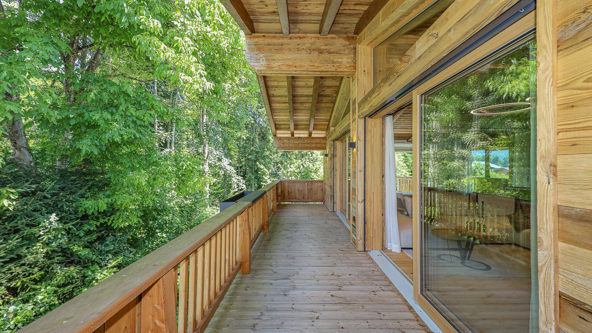 Langer Holzbalkon entlang der Fassade mit Blick ins Grüne und Zugang zu den Innenräumen.
