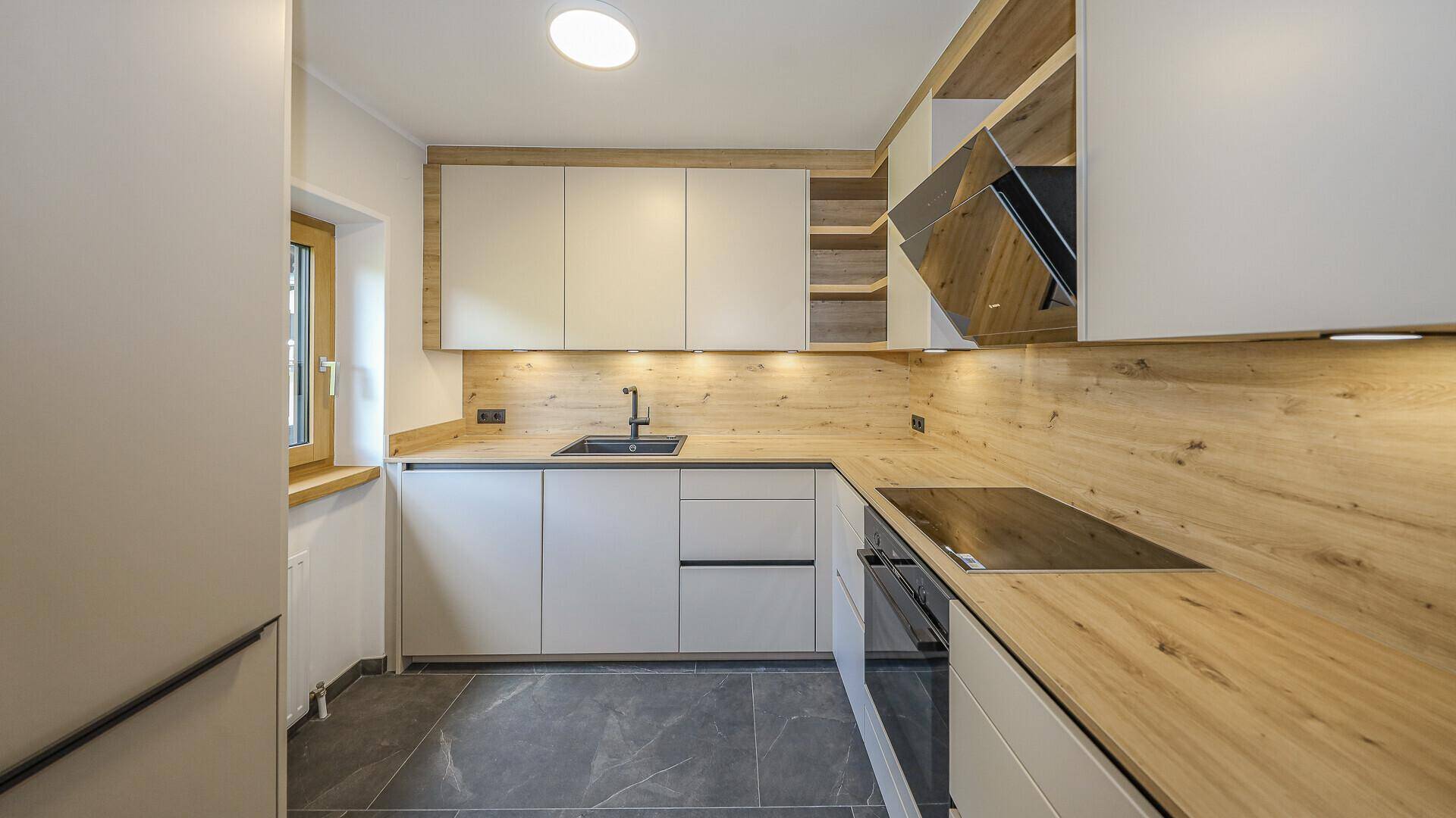 Moderne Küche mit hellen Schränken, Holzarbeitsplatten, dunklen Fliesen und Fenster.