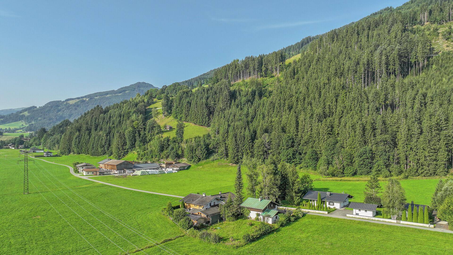Weitläufige Ansicht des Anwesens in einer sonnigen Berglandschaft mit grünen Wiesen und dichten Wäldern.