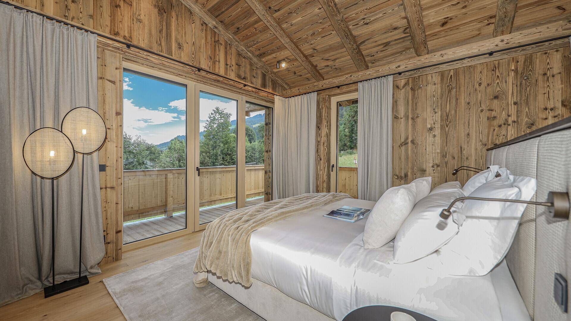 Helles Schlafzimmer mit Holzwänden, großem Bett und Zugang zu einem Balkon mit Bergblick.