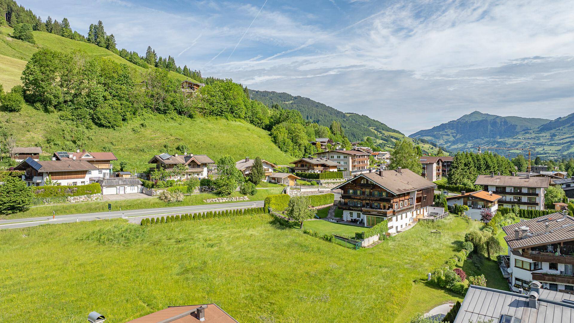 Blick über ein malerisches Dorf in einem grünen Tal, umgeben von bewaldeten Berghängen.