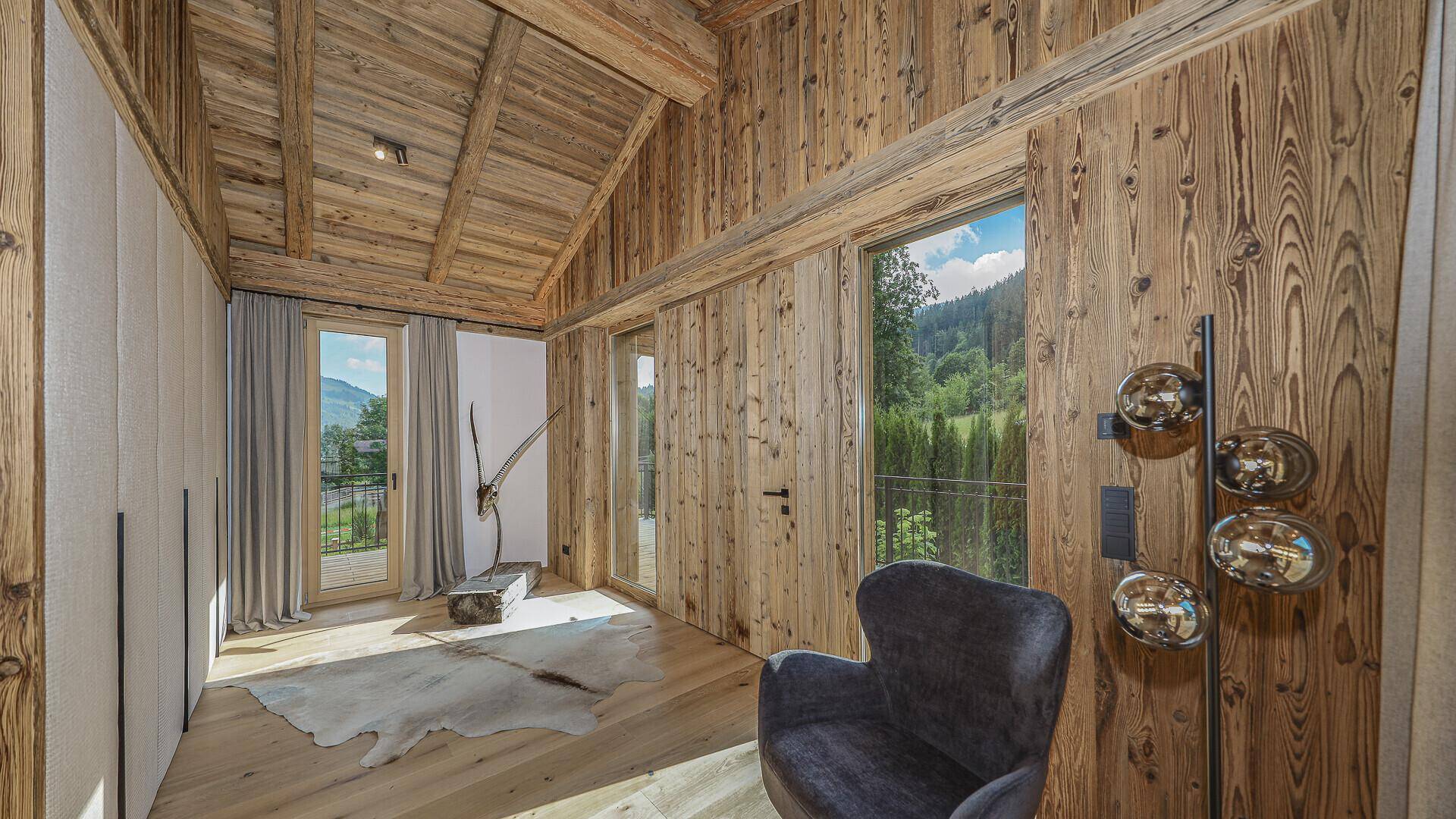 Rustikales Schlafzimmer mit Holzwänden, Holzbalkendecke und Bergblick durch große Fenster.
