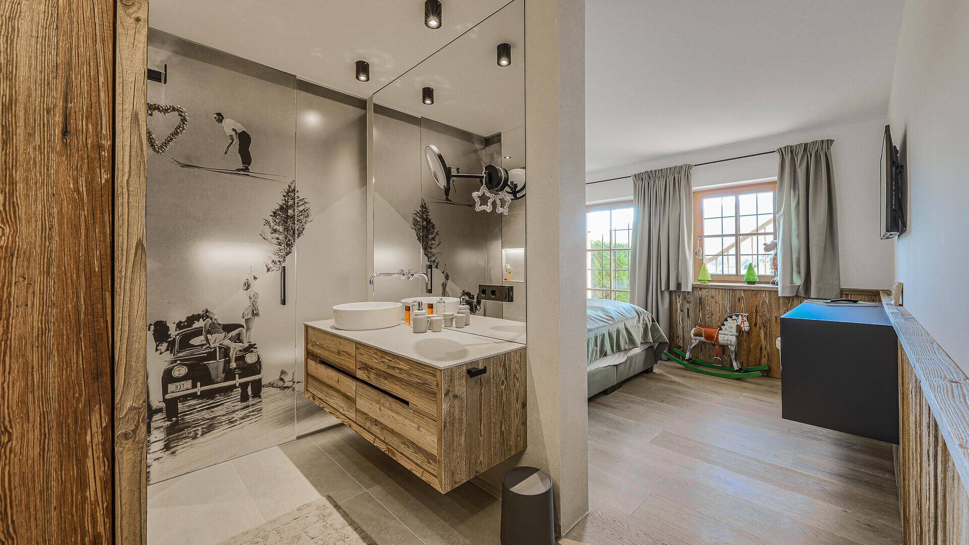 Schlafzimmer mit offenem Badezimmerbereich, Doppelwaschbecken und großer Spiegelfläche.