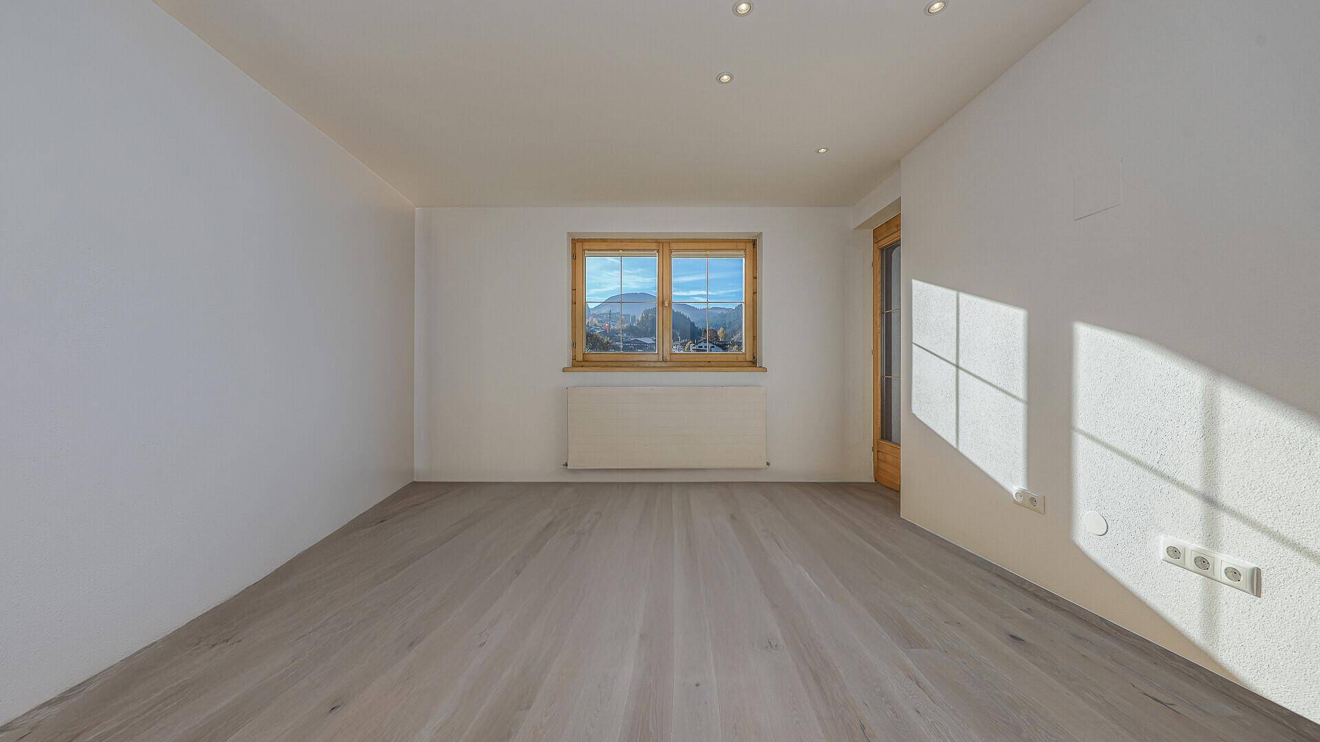 Helles, leeres Schlafzimmer mit Holzboden und Fenster mit Blick auf die umliegende Landschaft.