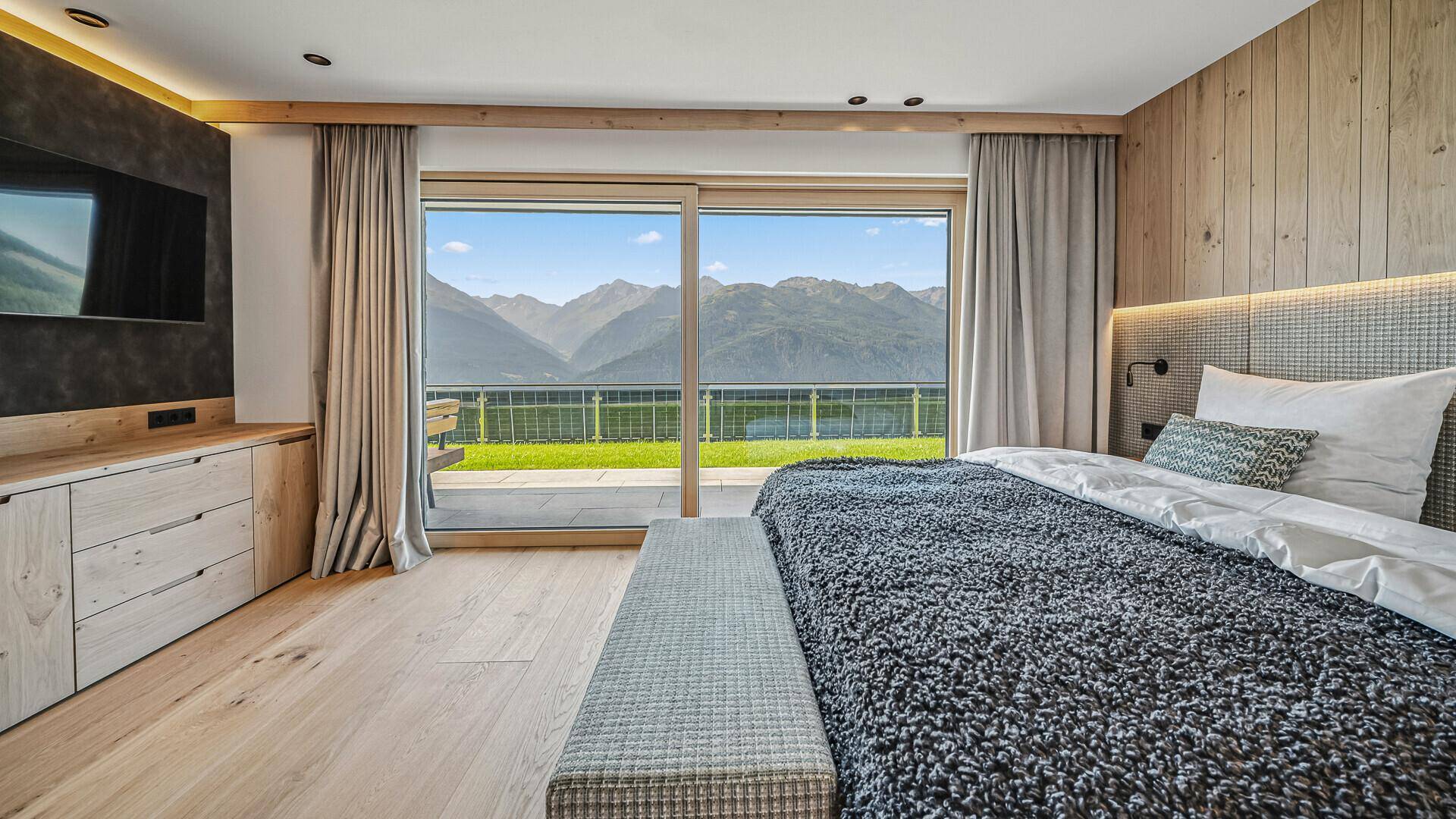 Helles Schlafzimmer mit Holzwand, großem Bett und Panoramablick auf die Berge.