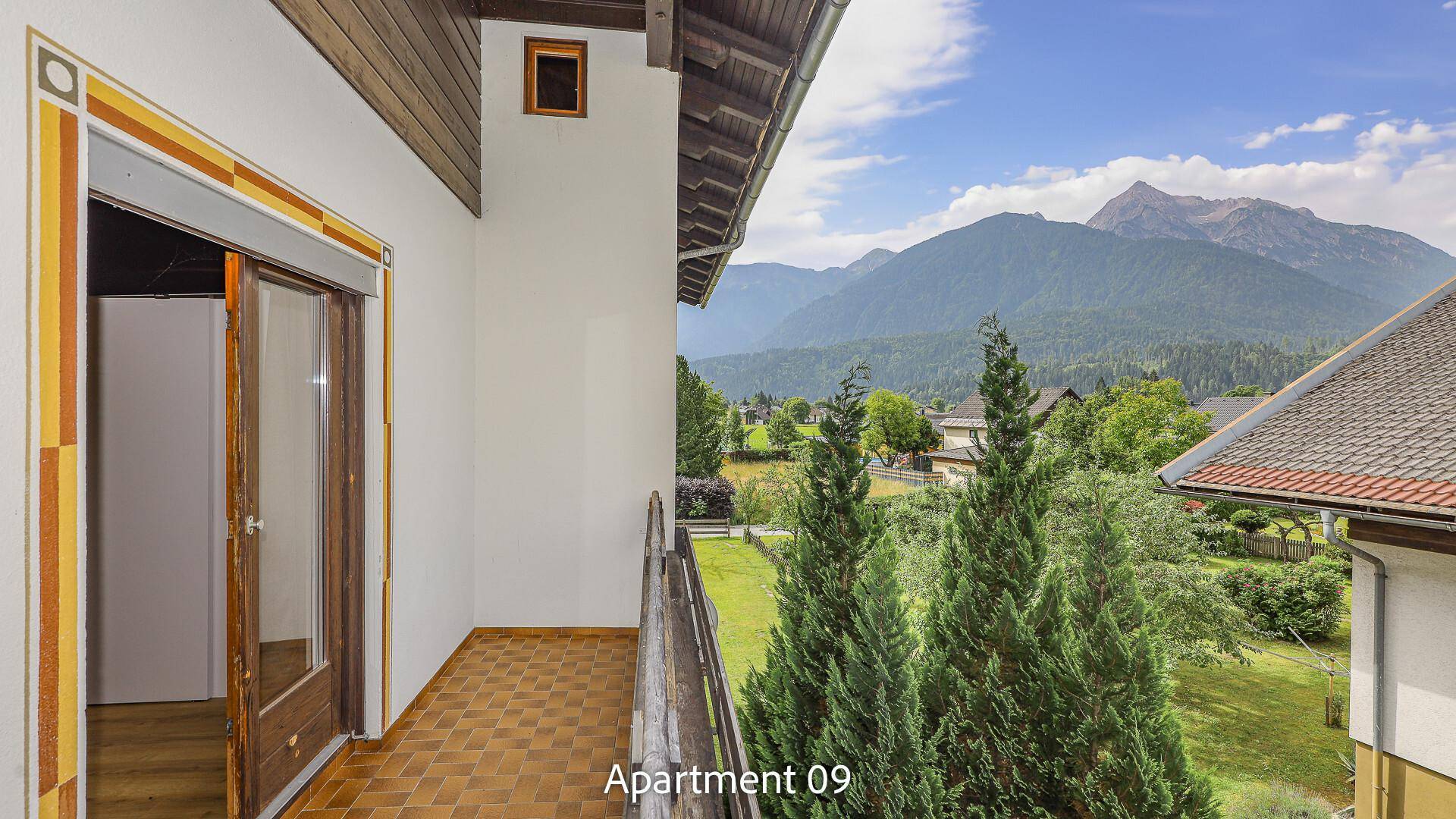 Balkon von Apartment 09 mit Fliesenboden und Holzgeländer, bietet einen weiten Blick auf die Berglandschaft.