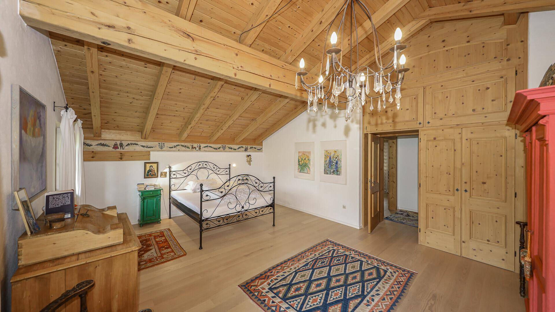 Geräumiges Schlafzimmer mit Holzbalkendecke, Holzboden und einem schmiedeeisernen Bett.
