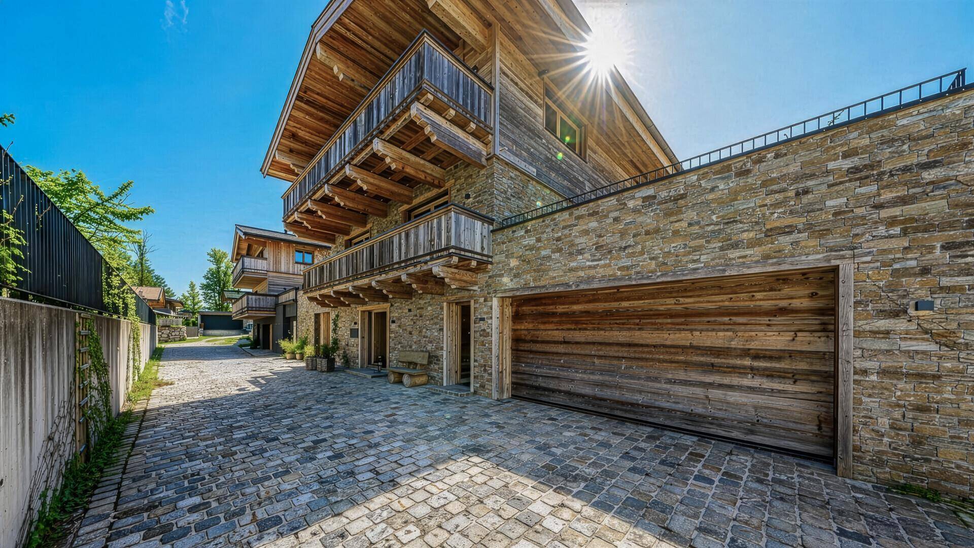 Alpines Haus mit Steinfassade, Holzverkleidung und großer Garageneinfahrt.