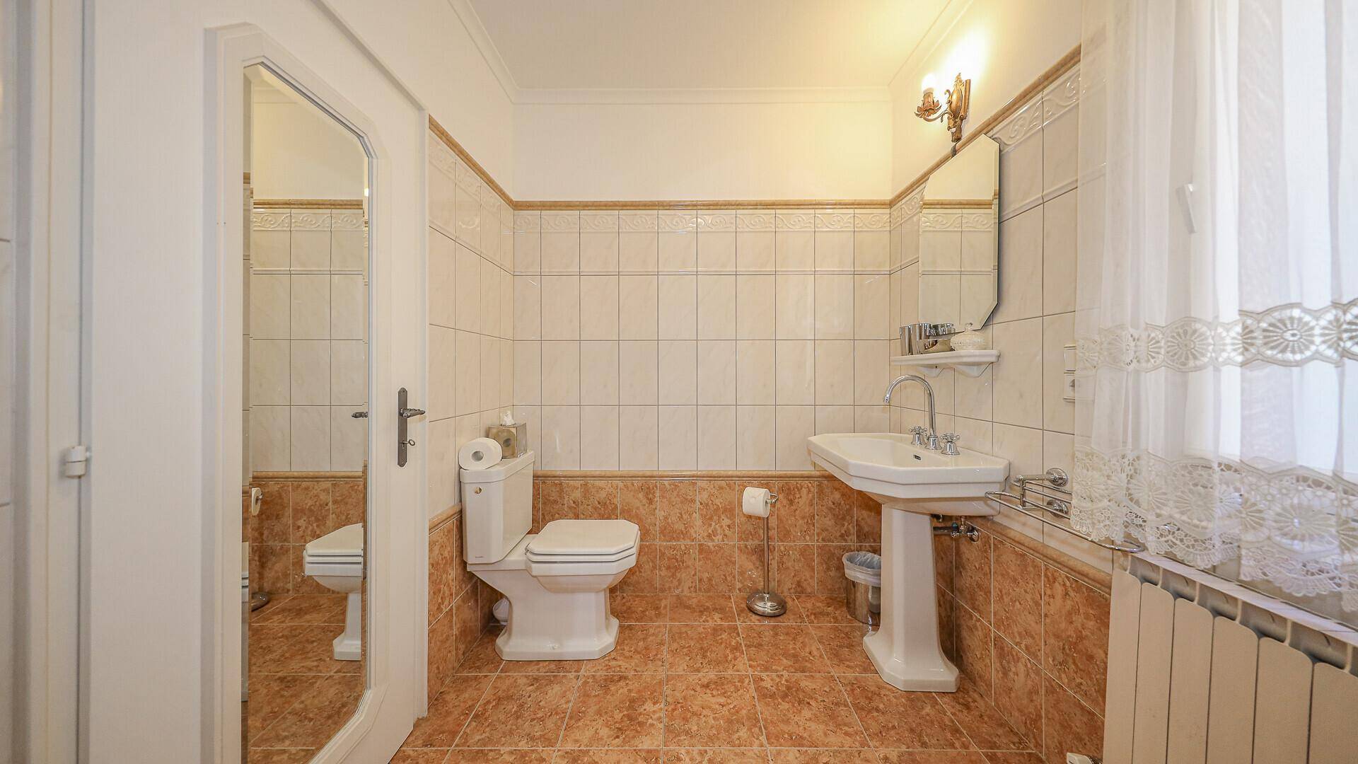 Badezimmer mit Waschbecken, Toilette und traditionellen Fliesen in Beige und Weiß.