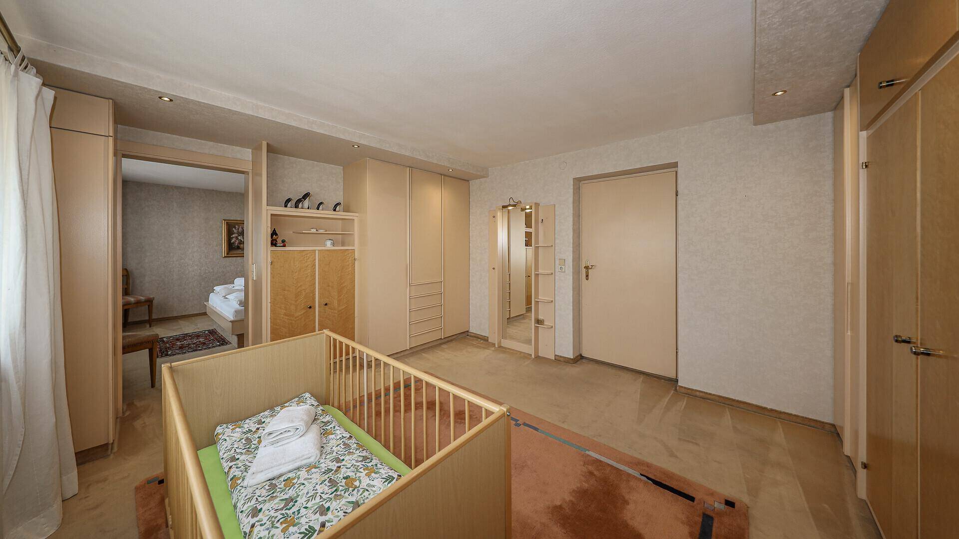Geräumiges Schlafzimmer mit Kinderbett, Einbauschränken und Zugang zu einem weiteren Raum.