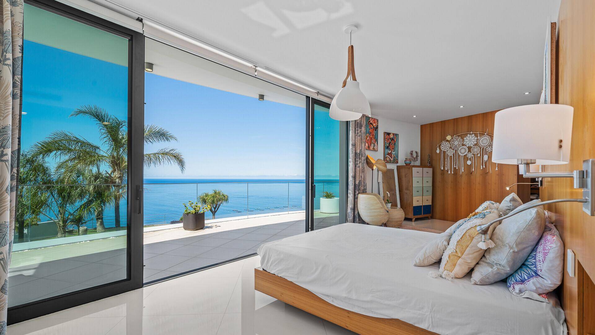 Helles Schlafzimmer mit Holzbett, Meerblick und Zugang zur Terrasse durch große Schiebetüren.