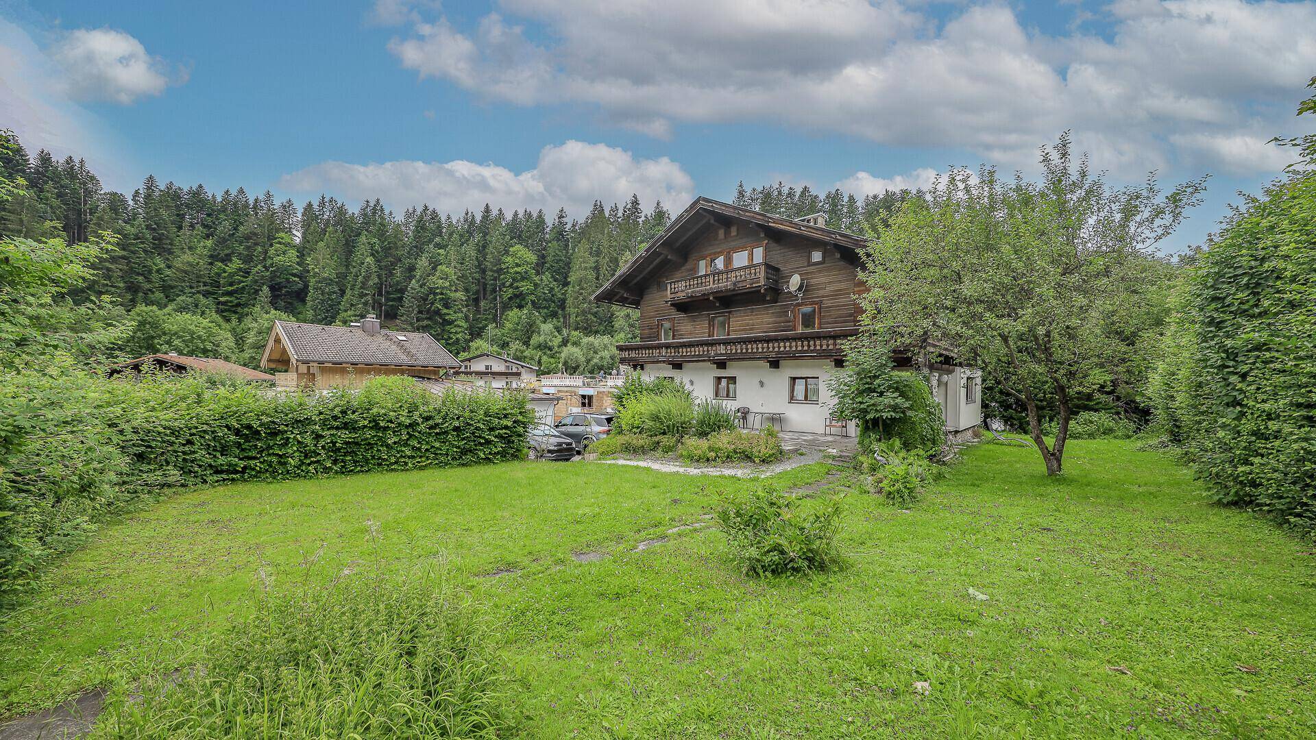 Traditionelles Holzhaus mit weißem Sockel und großem Garten umgeben von viel Grün.