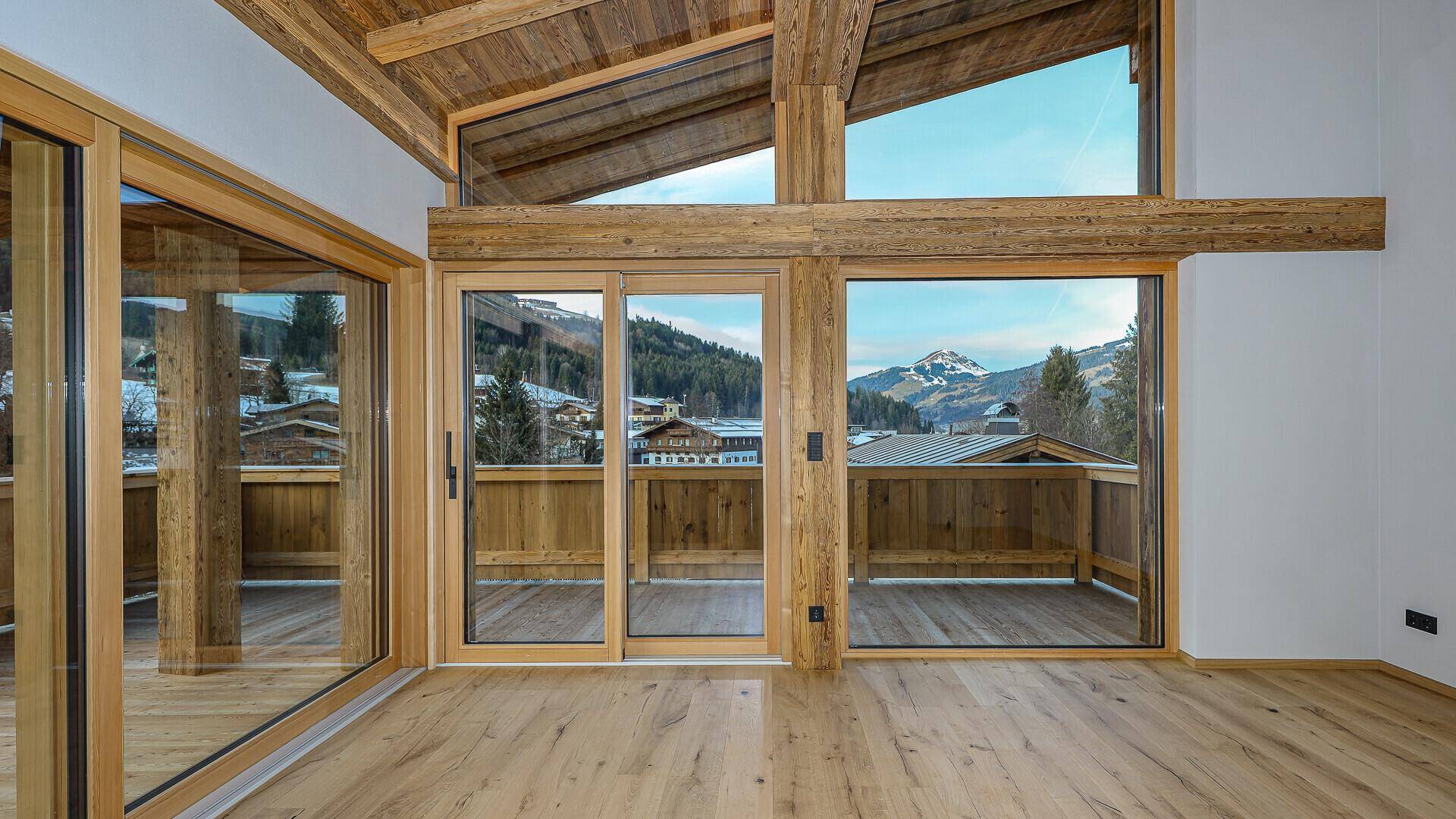 Heller Wohnbereich mit Holzbalkendecke und raumhohen Fenstern, die einen weiten Bergblick bieten.
