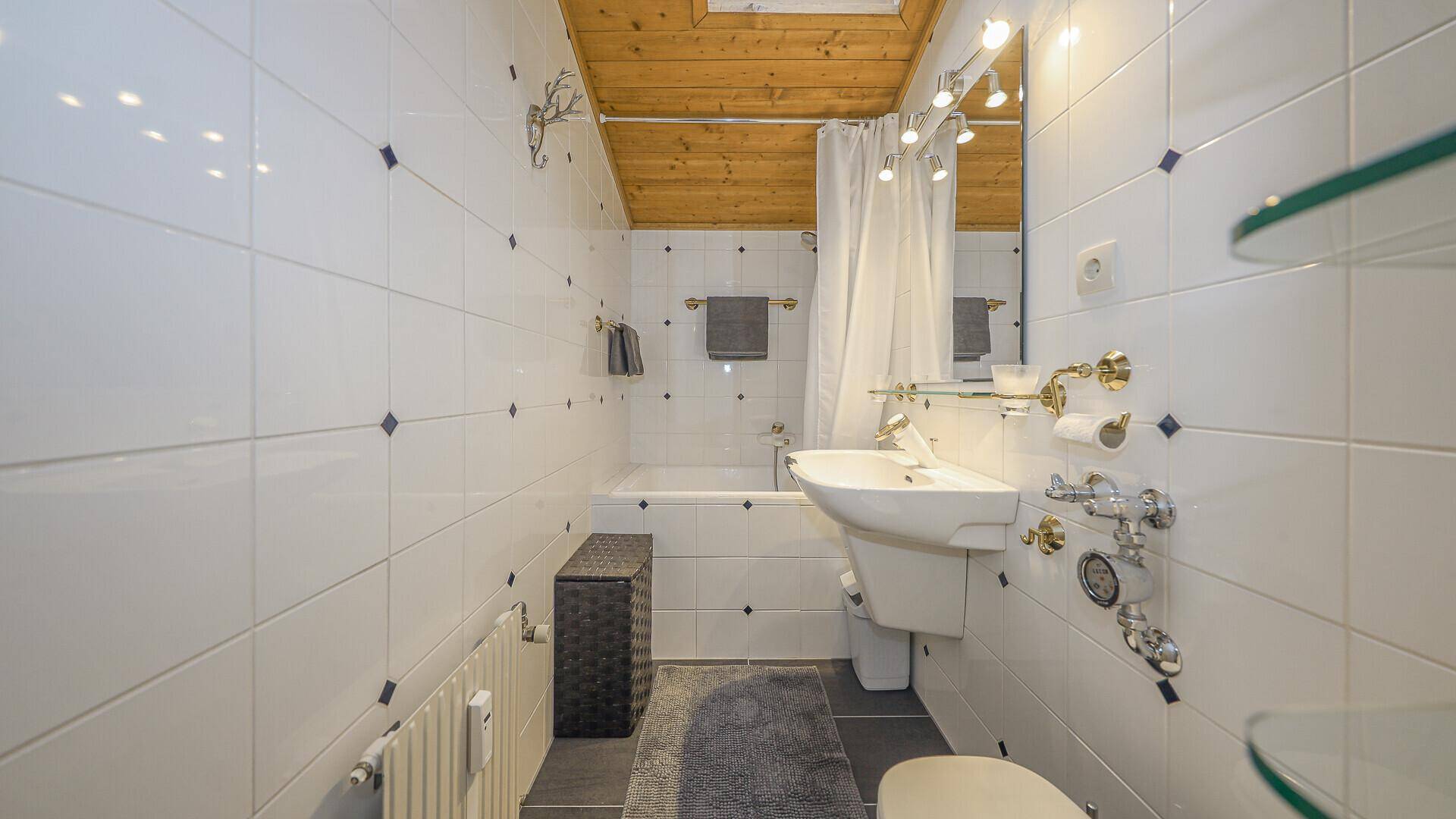 Helles Badezimmer mit weißen Fliesen, Badewanne mit Duschvorhang und Holzdecke.