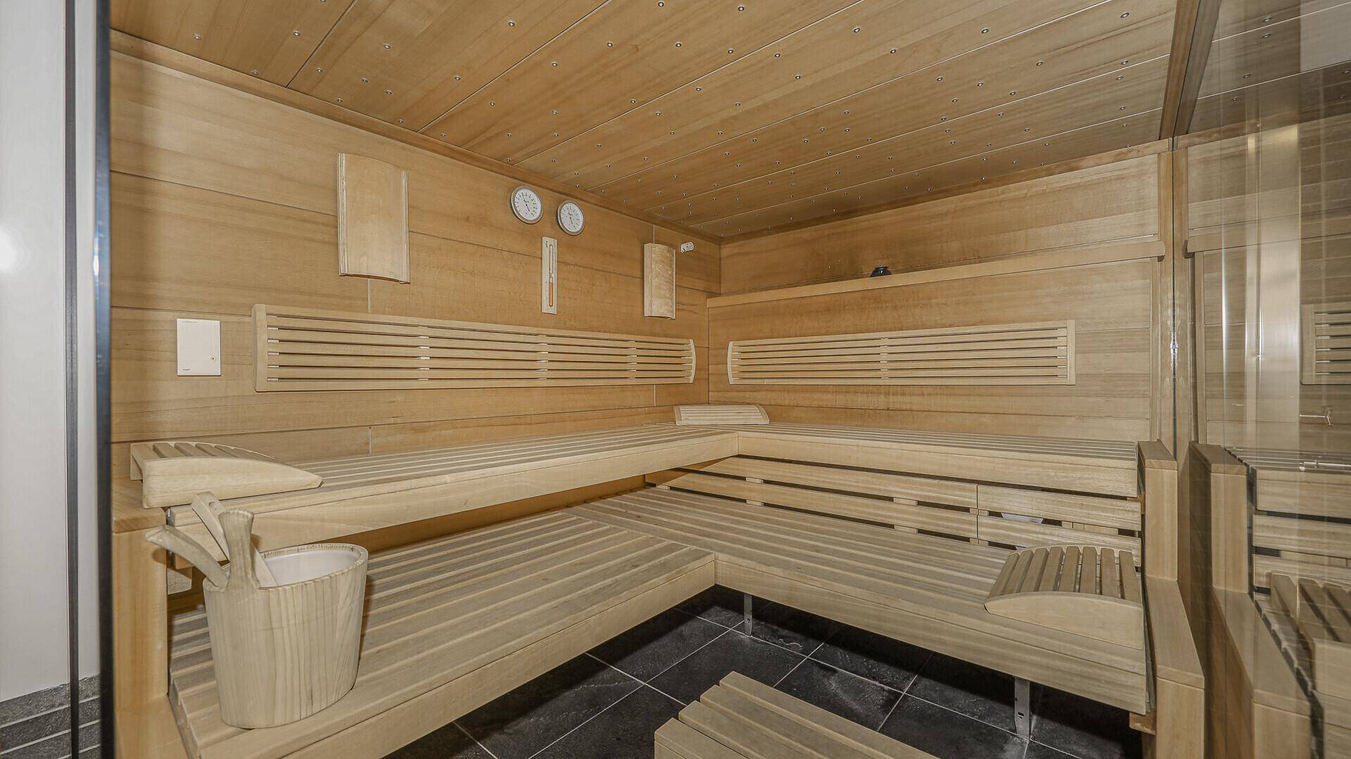 Geräumige Holzsauna mit mehreren Bänken und traditionellem Saunaeimer für Entspannung.