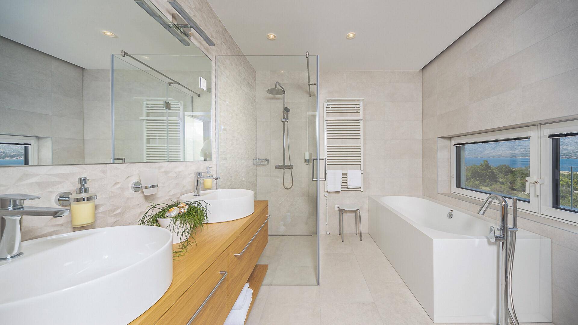 Elegantes Badezimmer mit Badewanne, begehbarer Dusche, Doppelwaschbecken und Fenster mit Meerblick.