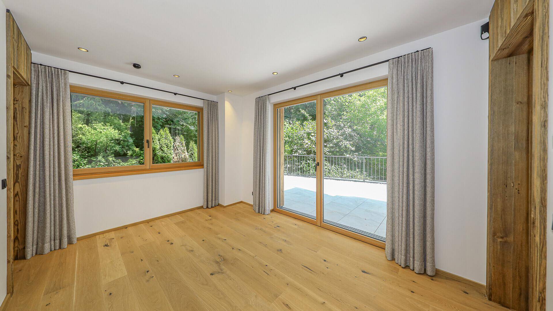 Helles Schlafzimmer mit Holzboden und großen Fenstern mit Blick ins Grüne.