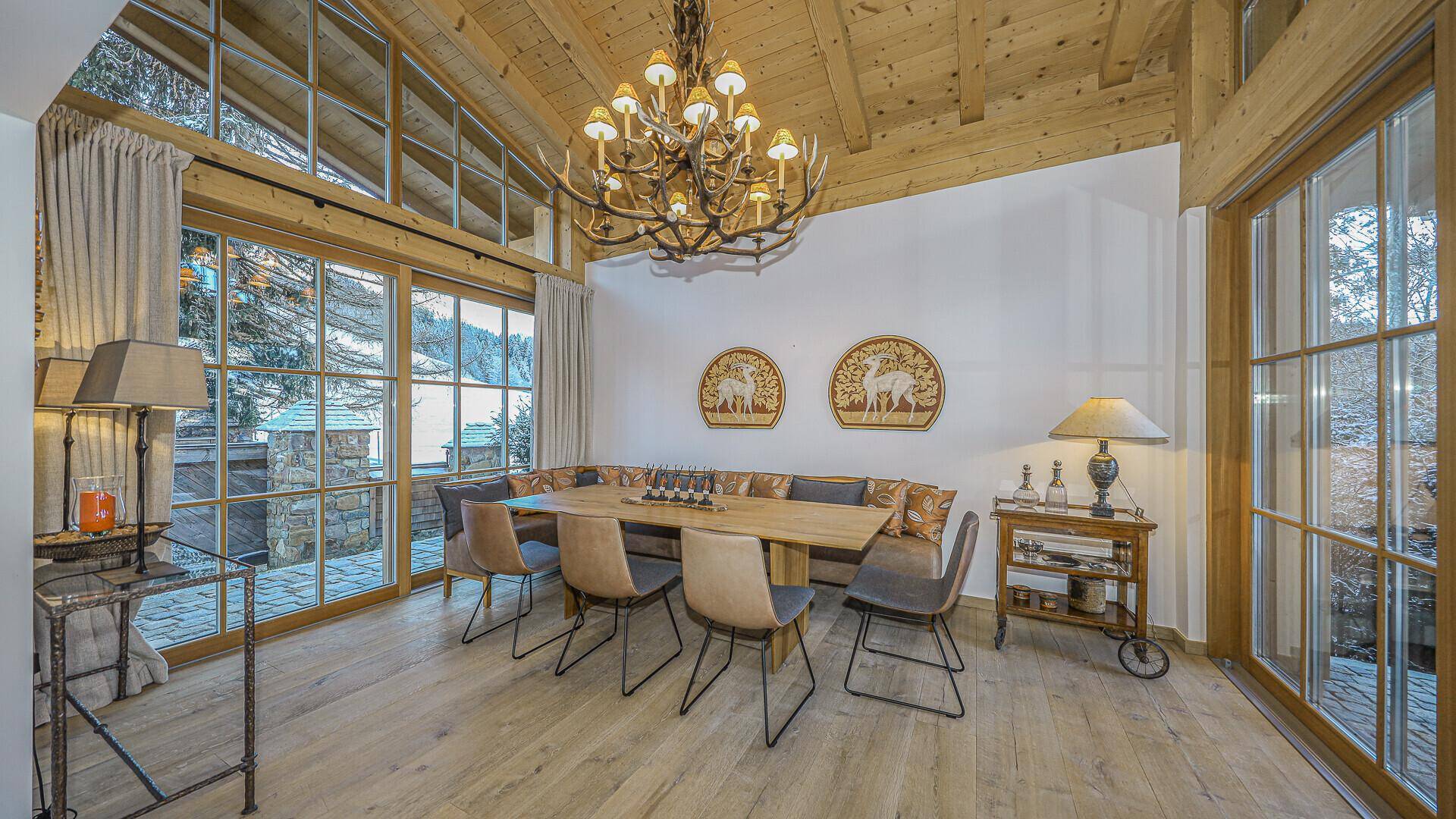 Heller Essbereich mit hohen Fenstern, Holzbalkendecke und großem Esstisch im alpinen Design.