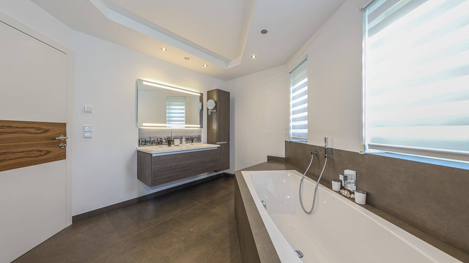 Stilvolles Badezimmer mit schwebendem Doppelwaschbecken, beleuchtetem Spiegel und großer Badewanne.