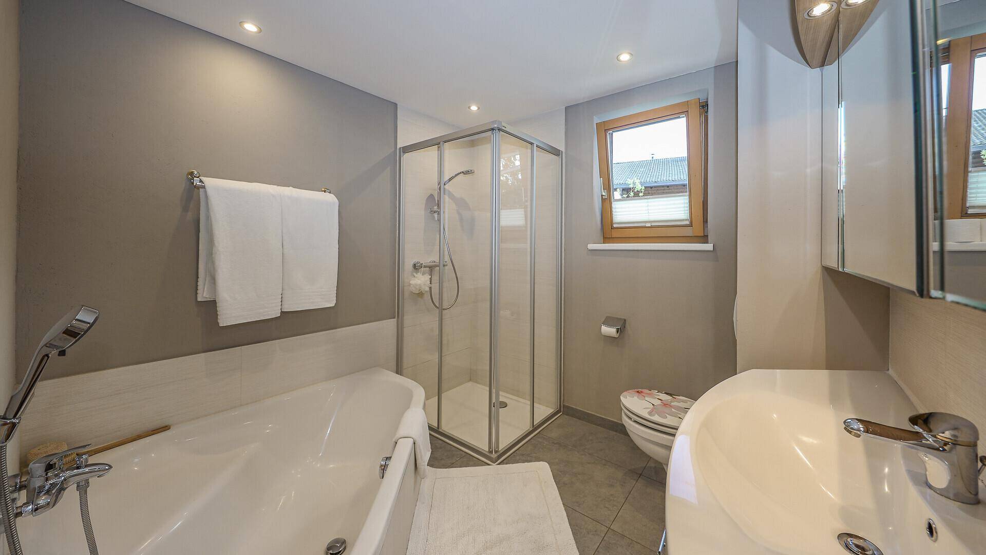 Modernes Badezimmer mit Badewanne, Duschkabine, WC und Fenster.
