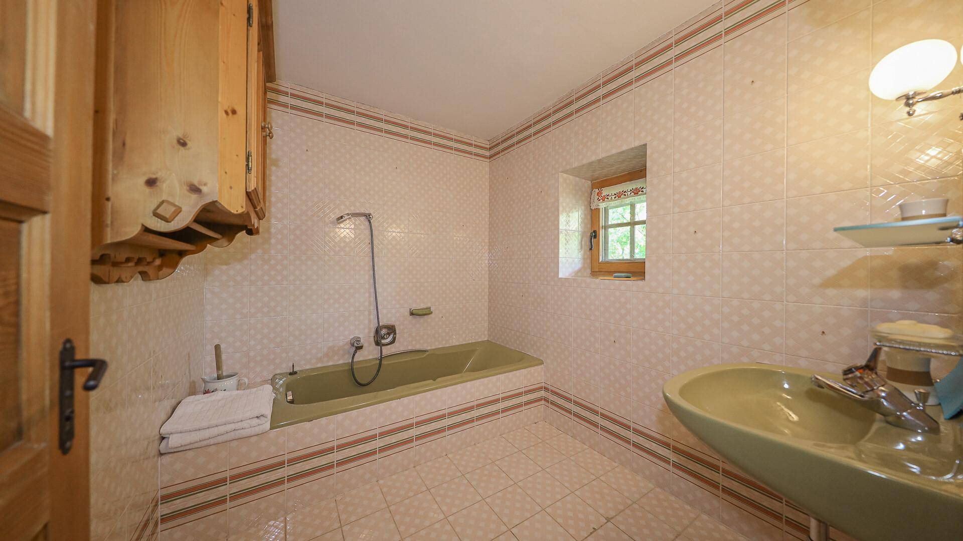 Badezimmer mit Badewanne, Waschbecken und traditionellen Fliesen, bietet Blick ins Grüne.