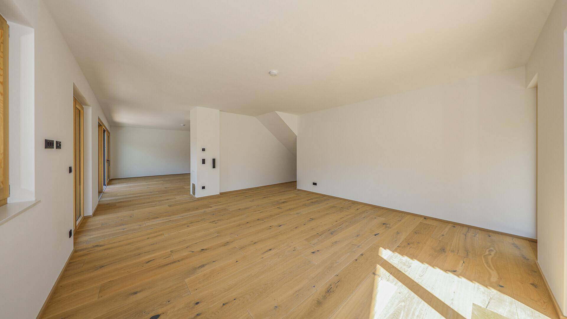 Heller Raum mit Holzboden, Dachschräge und Zugang zu einem Balkon, ideal als Wohnbereich.
