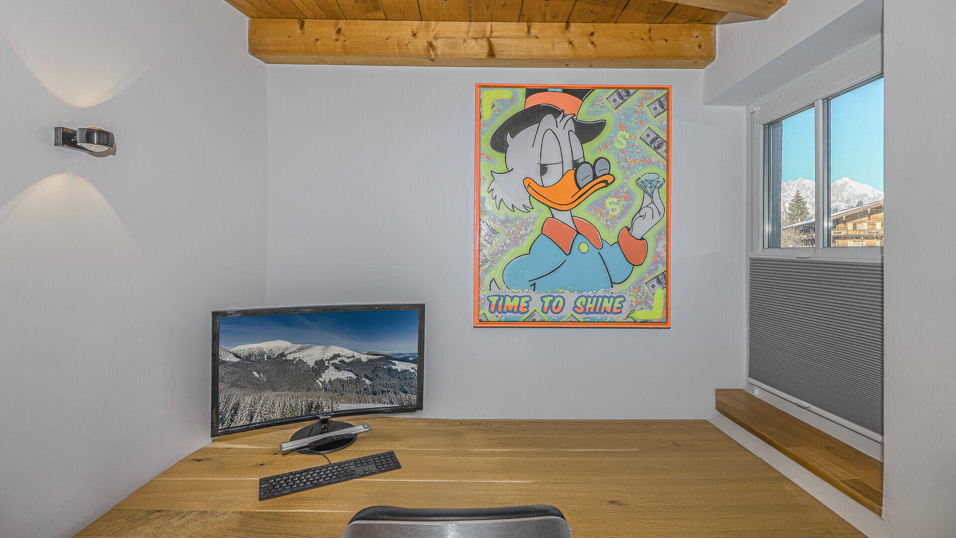 Funktionaler Arbeitsbereich mit Schreibtisch, Computer und einem Fenster, das einen Blick auf die Berge freigibt.