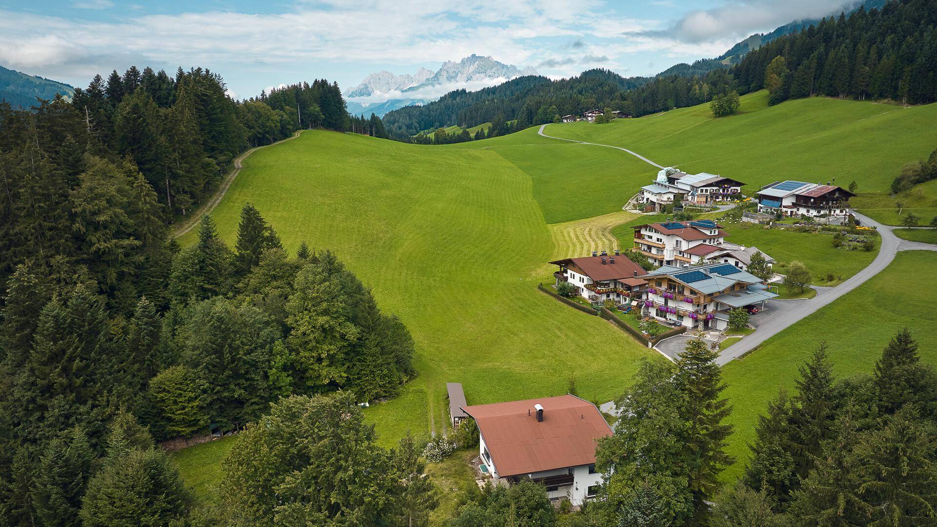 Luftaufnahme einer Siedlung von Häusern in einer malerischen Berglandschaft mit viel Grün.