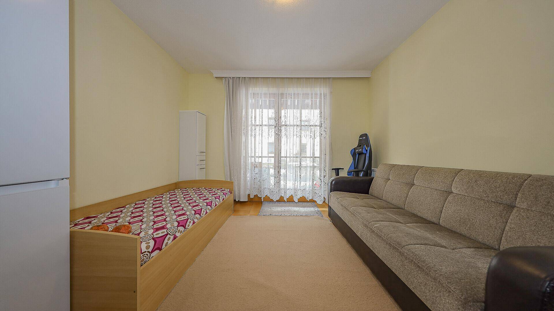 Helles Schlafzimmer mit Sofa, Einzelbett und Zugang zum Balkon.