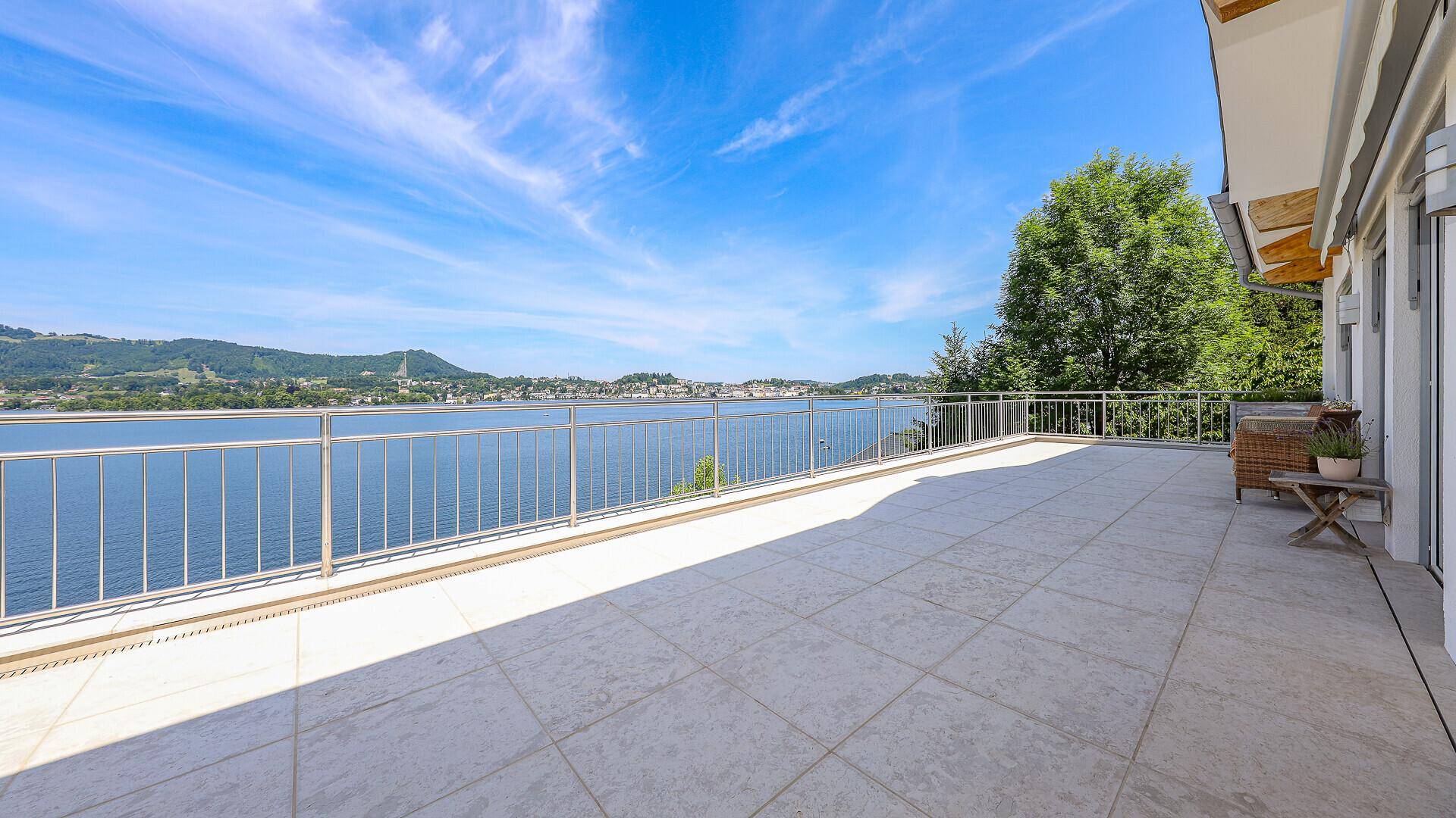 Sonnige Terrasse mit Fliesenboden und atemberaubendem Panoramablick auf den See und die Berge.
