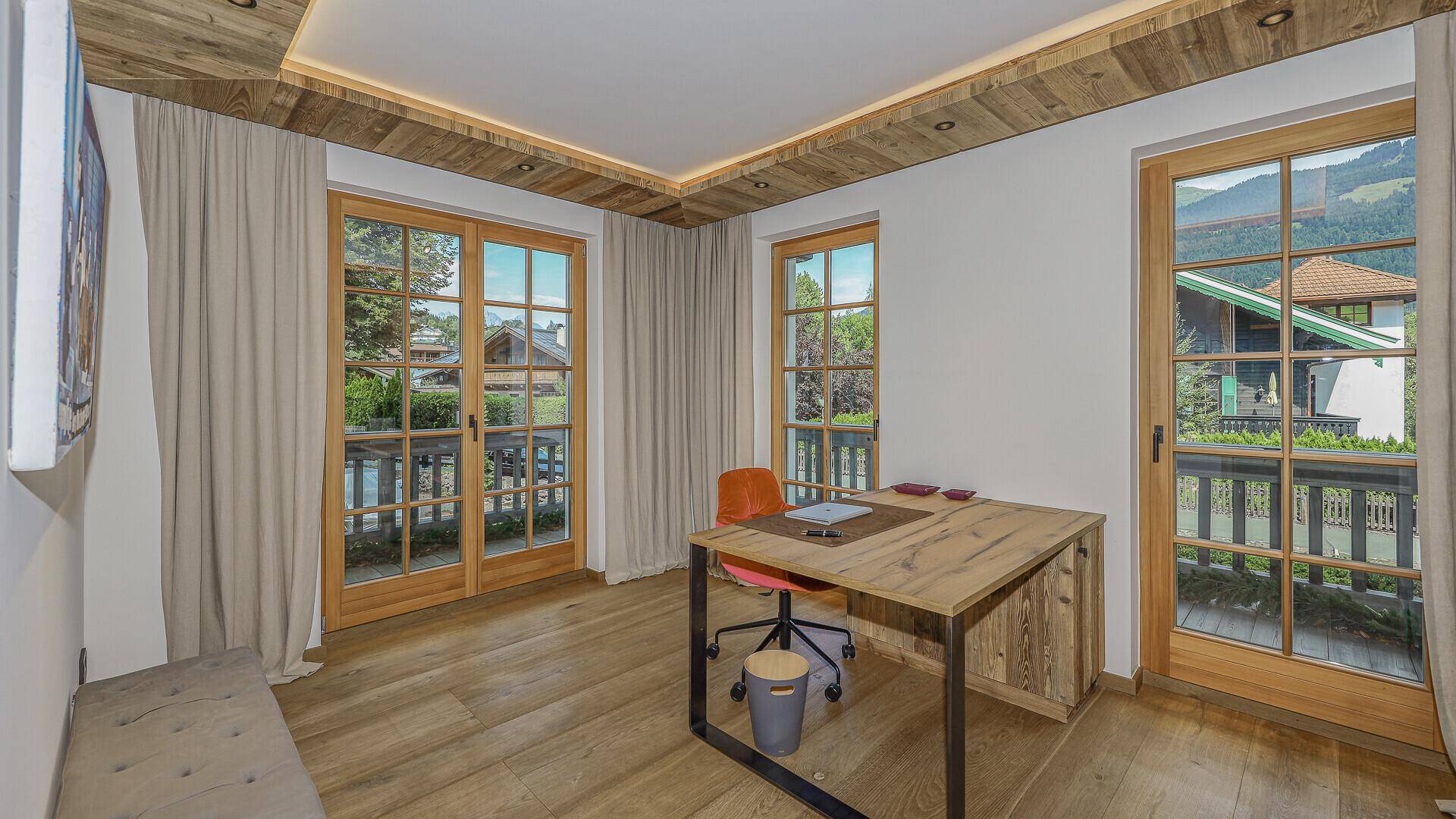 Helles Arbeitszimmer mit Holzboden, großzügigen Fenstern und Zugang zu einem Balkon.