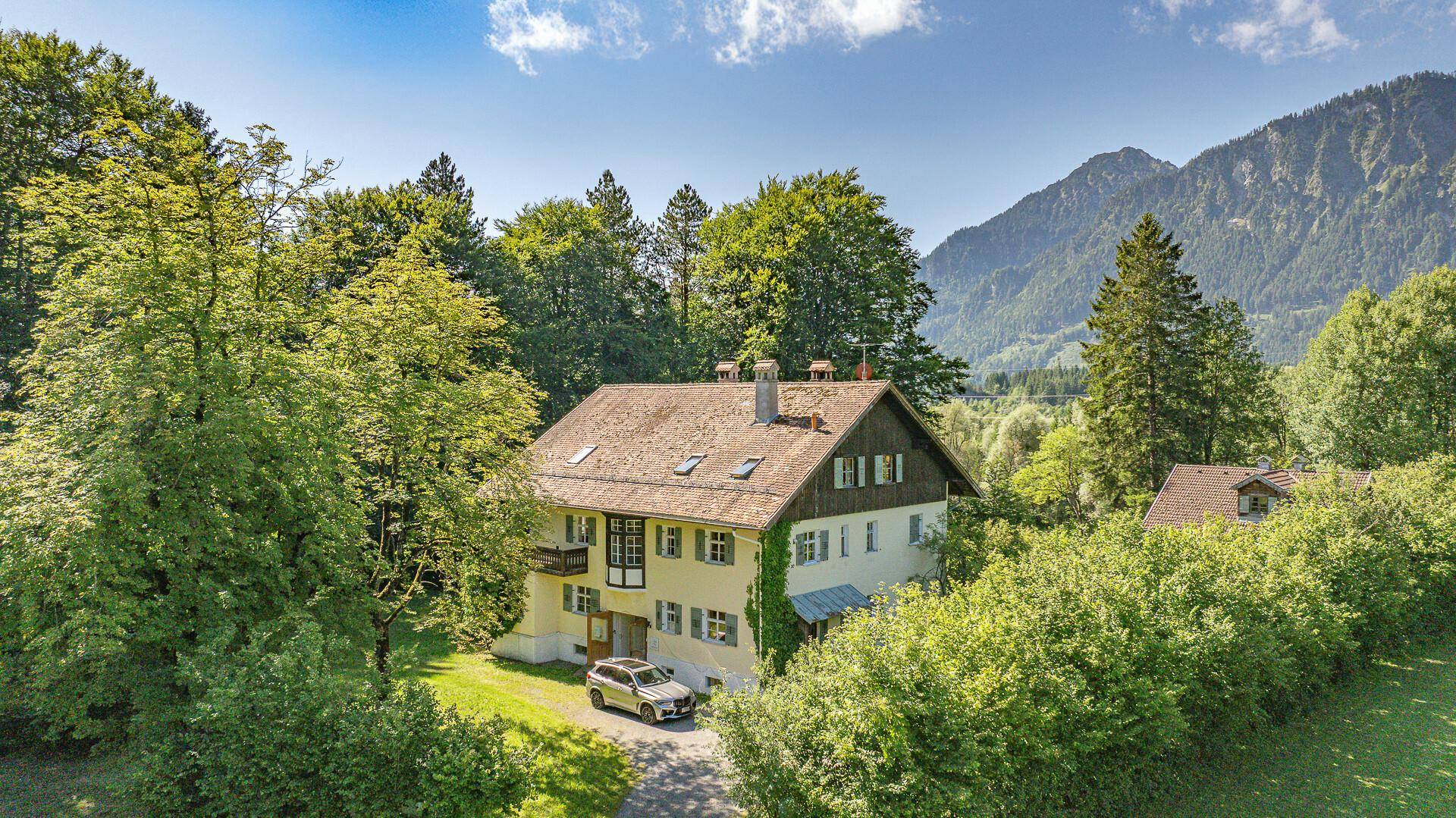 Haus umgeben von üppiger Natur mit Bergblick und einem Auto auf dem Kiesweg.