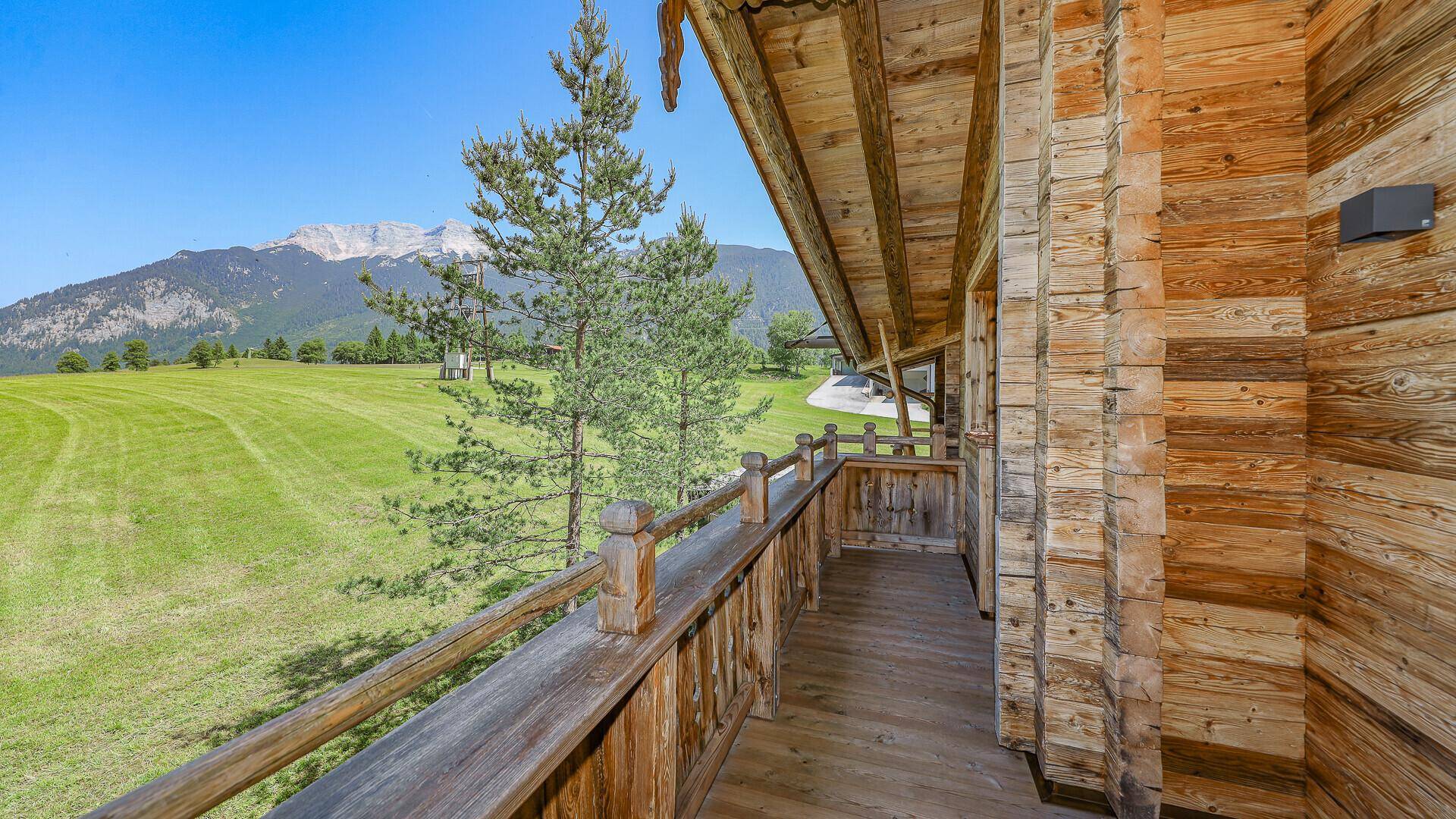 Geräumiger Holzbalkon mit traditionellem Geländer und weitem Blick auf grüne Wiesen und Berge.